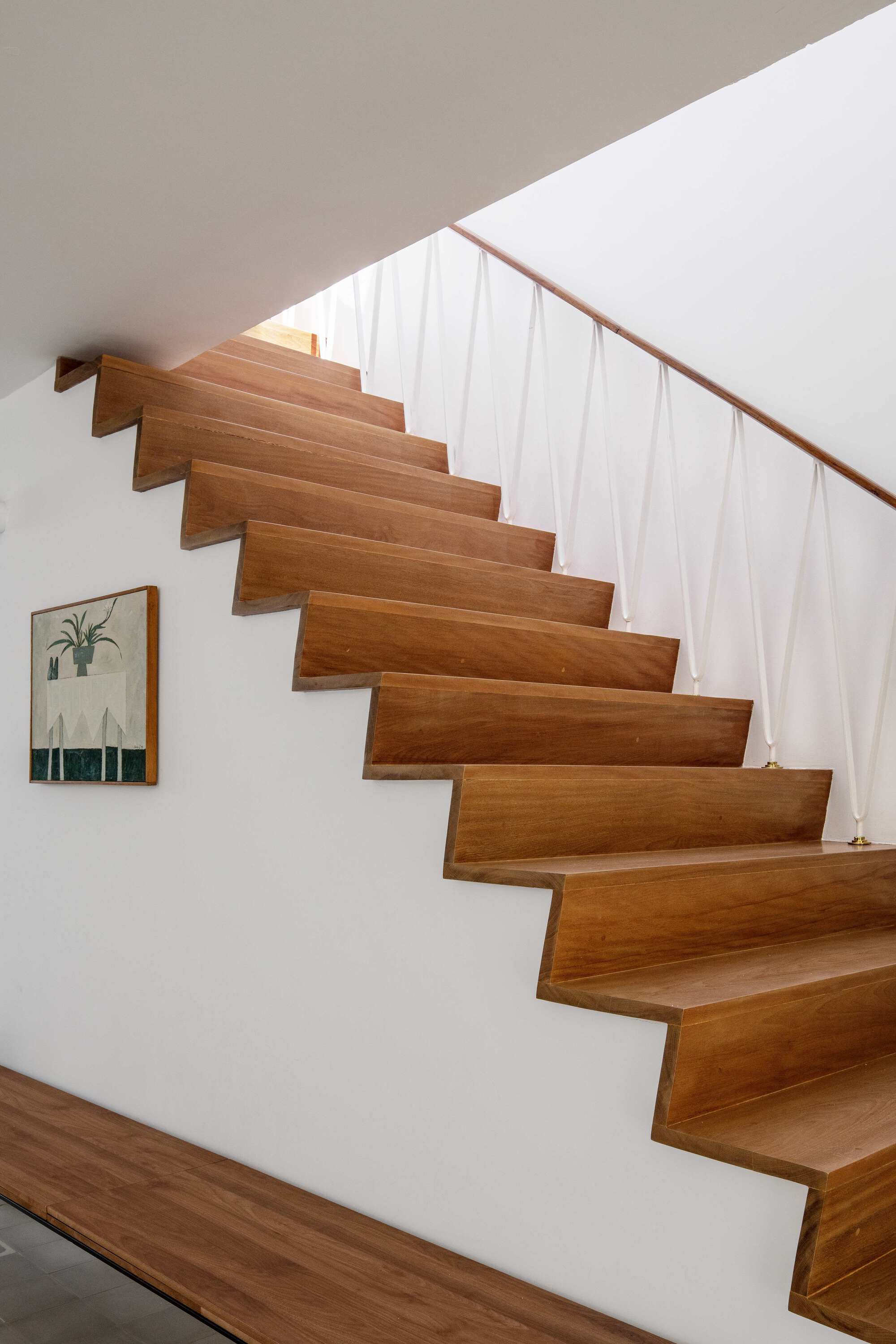 Close view of folded timber stair treads with a slim white rod balustrade and a small framed plant picture on the wall