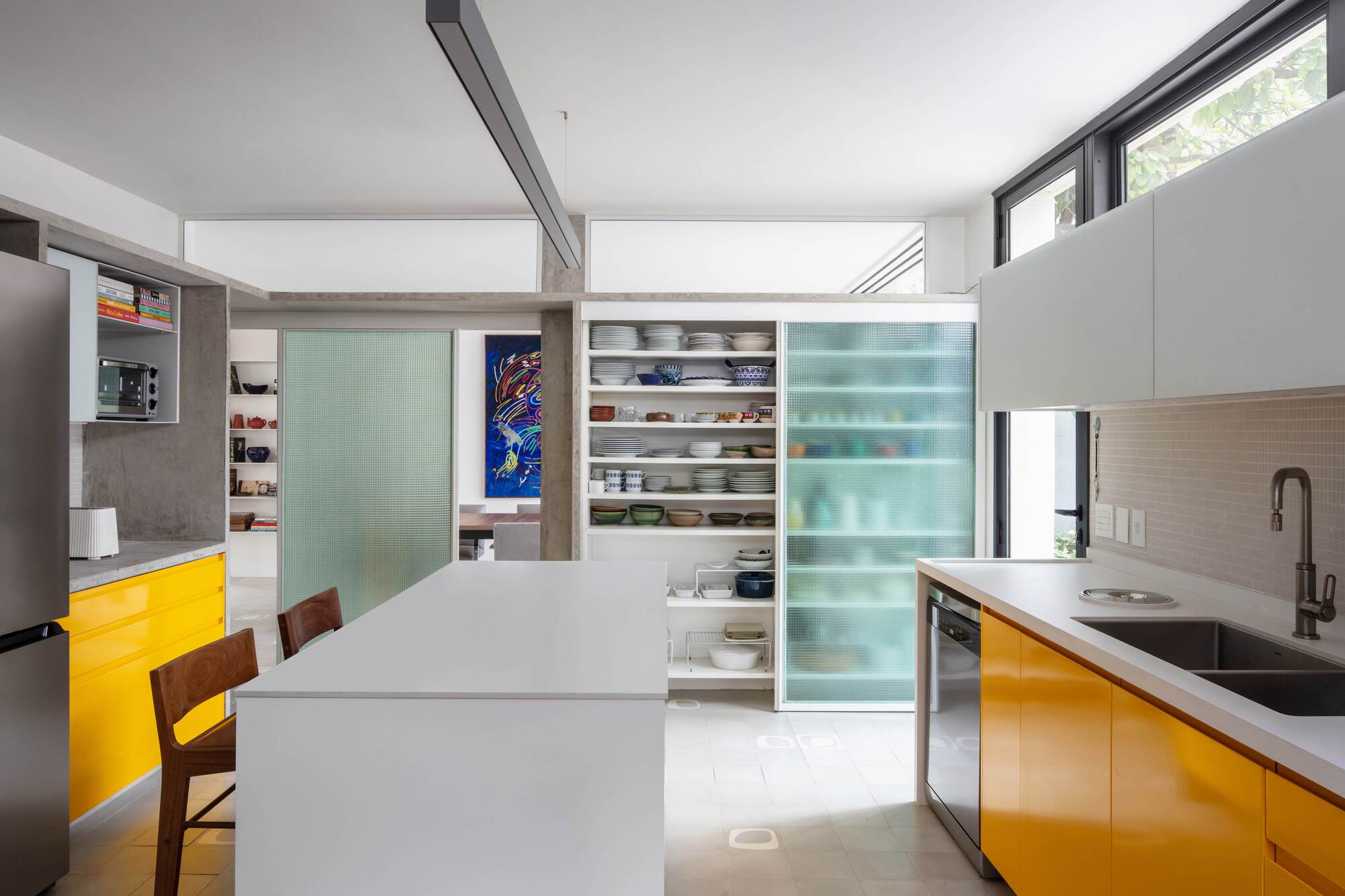 Kitchen with a white island, yellow cabinets and open dish shelving beside a ribbed green glass sliding panel in daylight