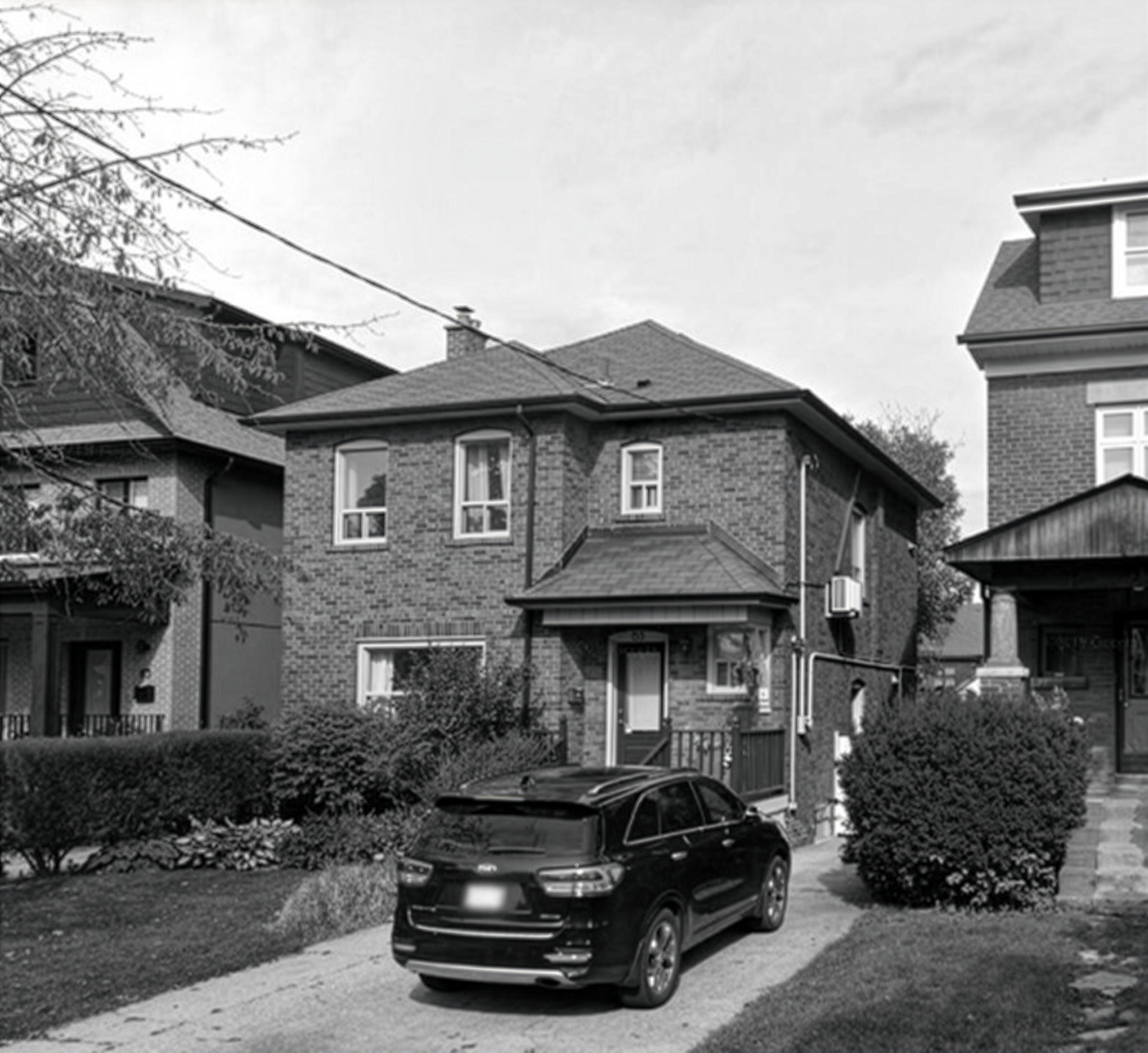 Black and white photo of the original two-storey brick house with a hipped roof and an SUV parked in the driveway