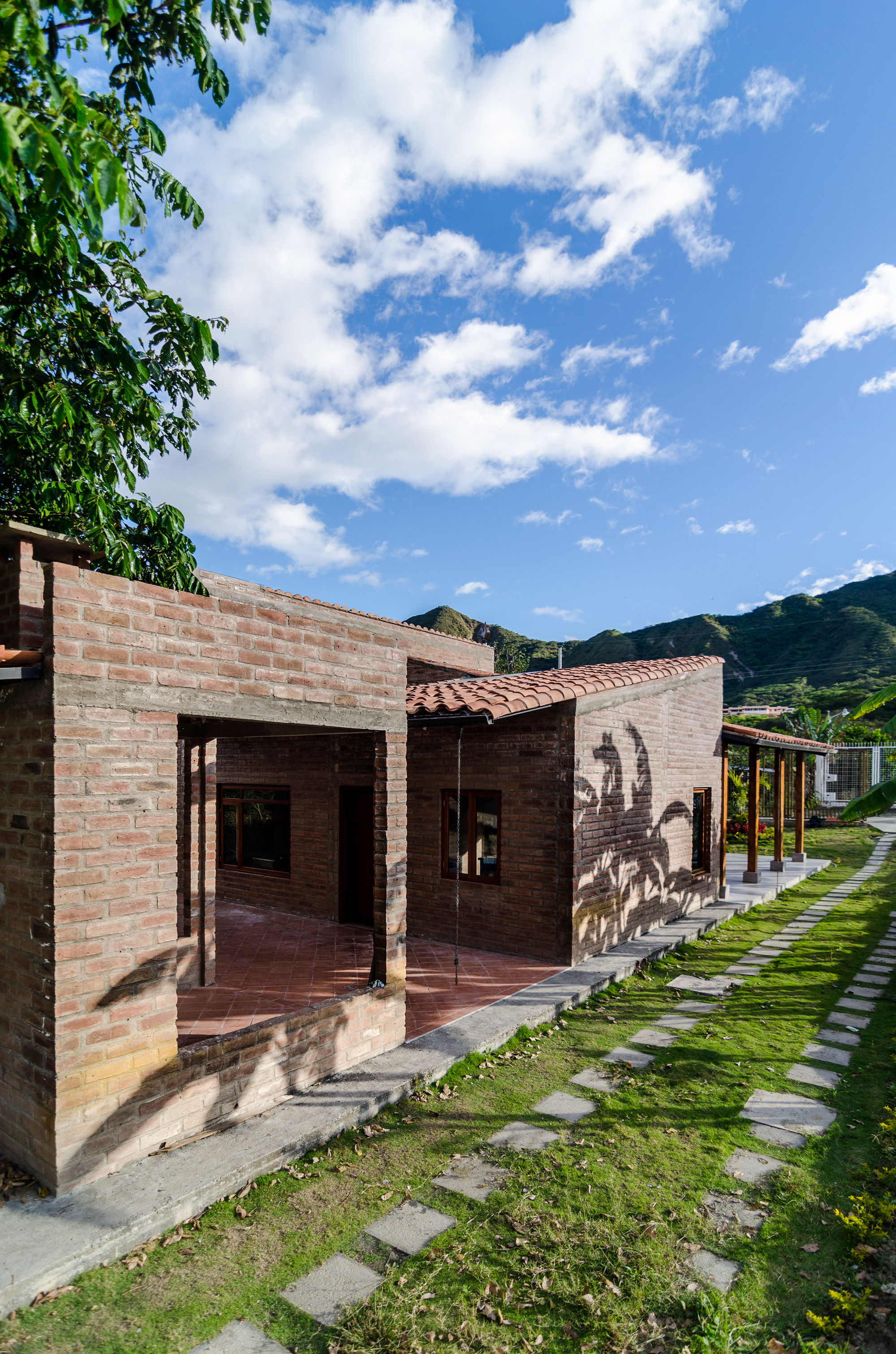 Side view of brick walls and a clay tile roof beside a stepping stone path, with green hills and cloud behind