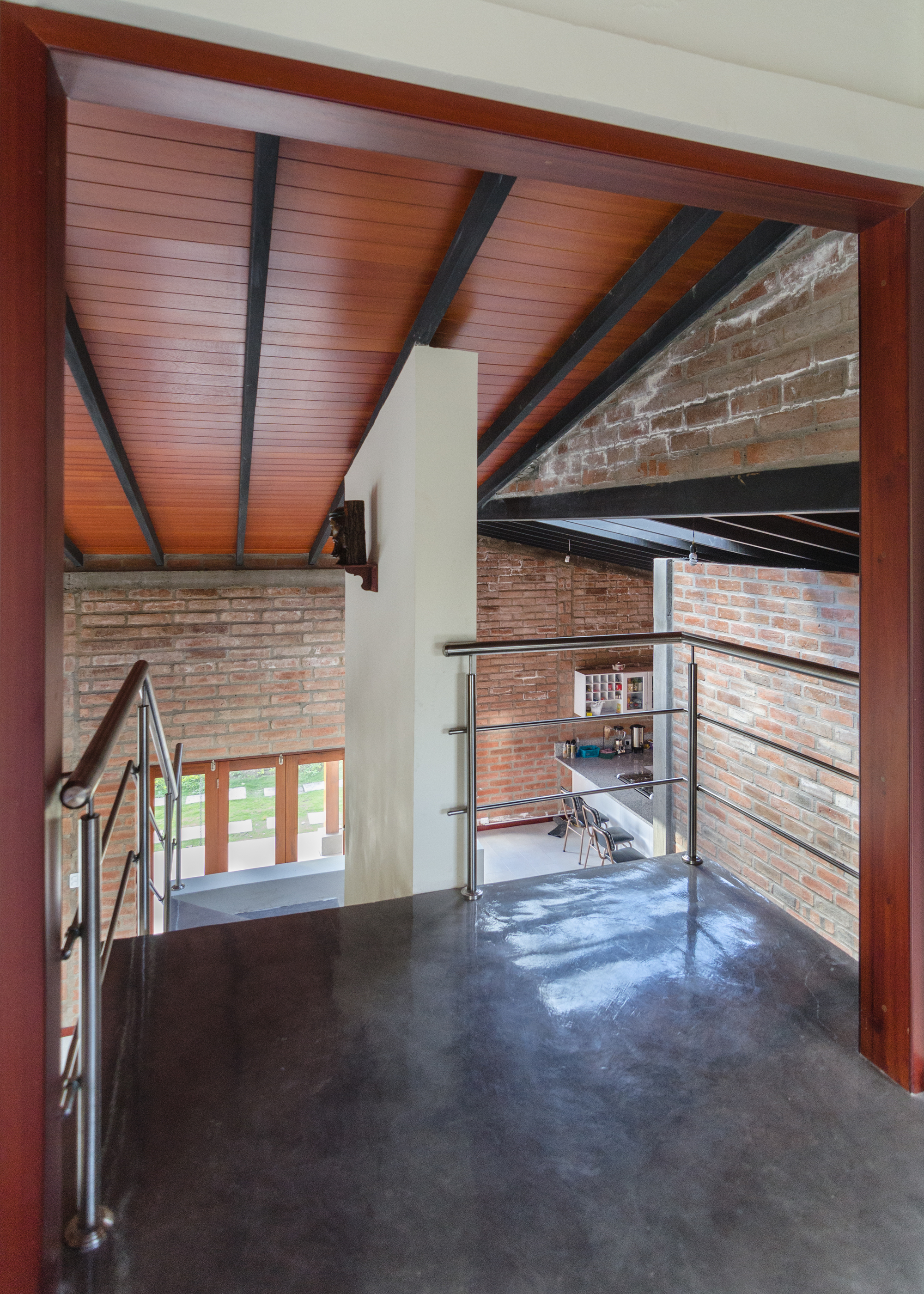 View through a timber door frame to a steel-railed landing, dark polished floor, brick walls and a dark-beamed timber ceiling