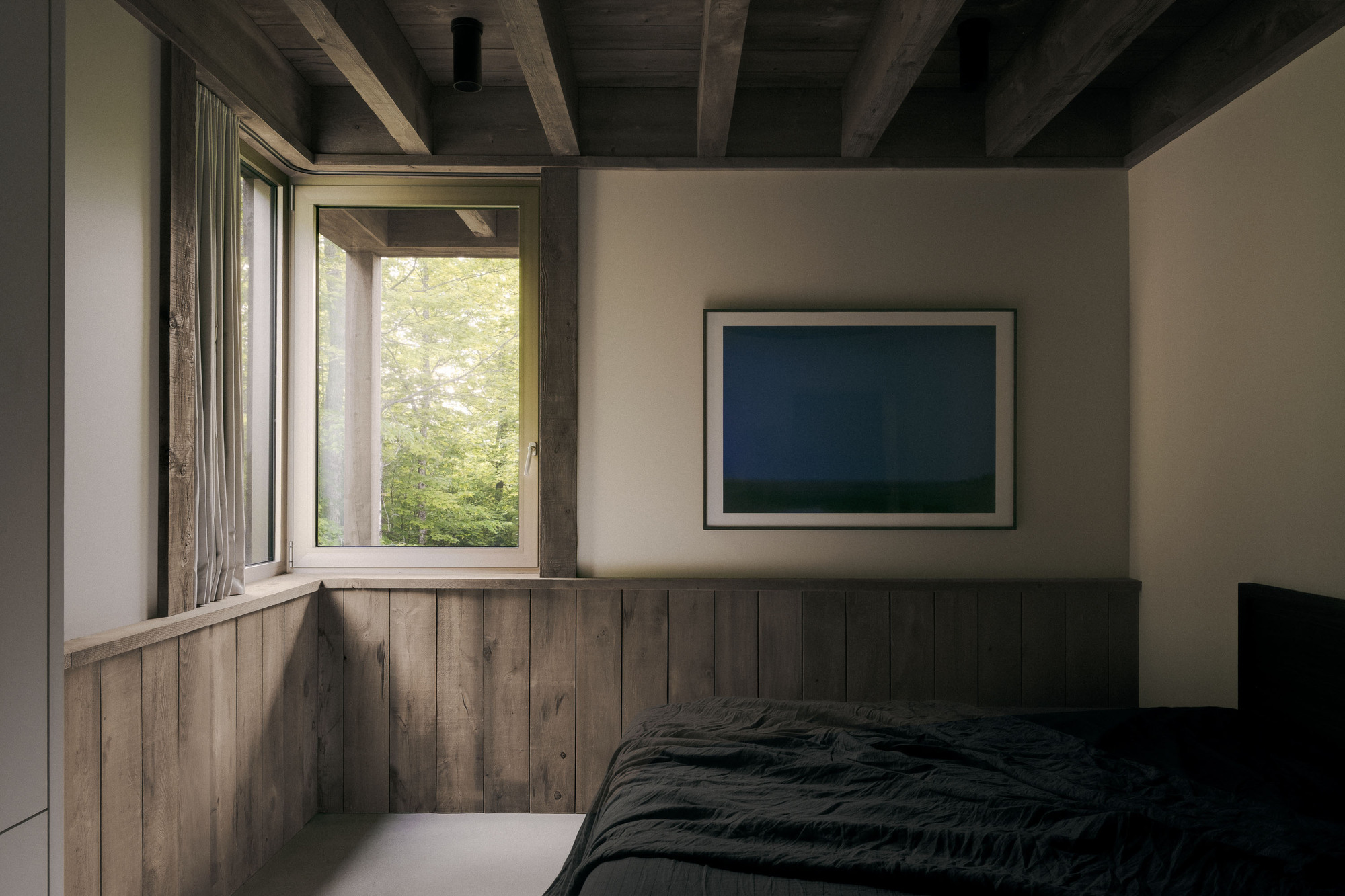 Bedroom corner with reclaimed plank wainscot, a framed blue artwork and a corner window looking into green foliage