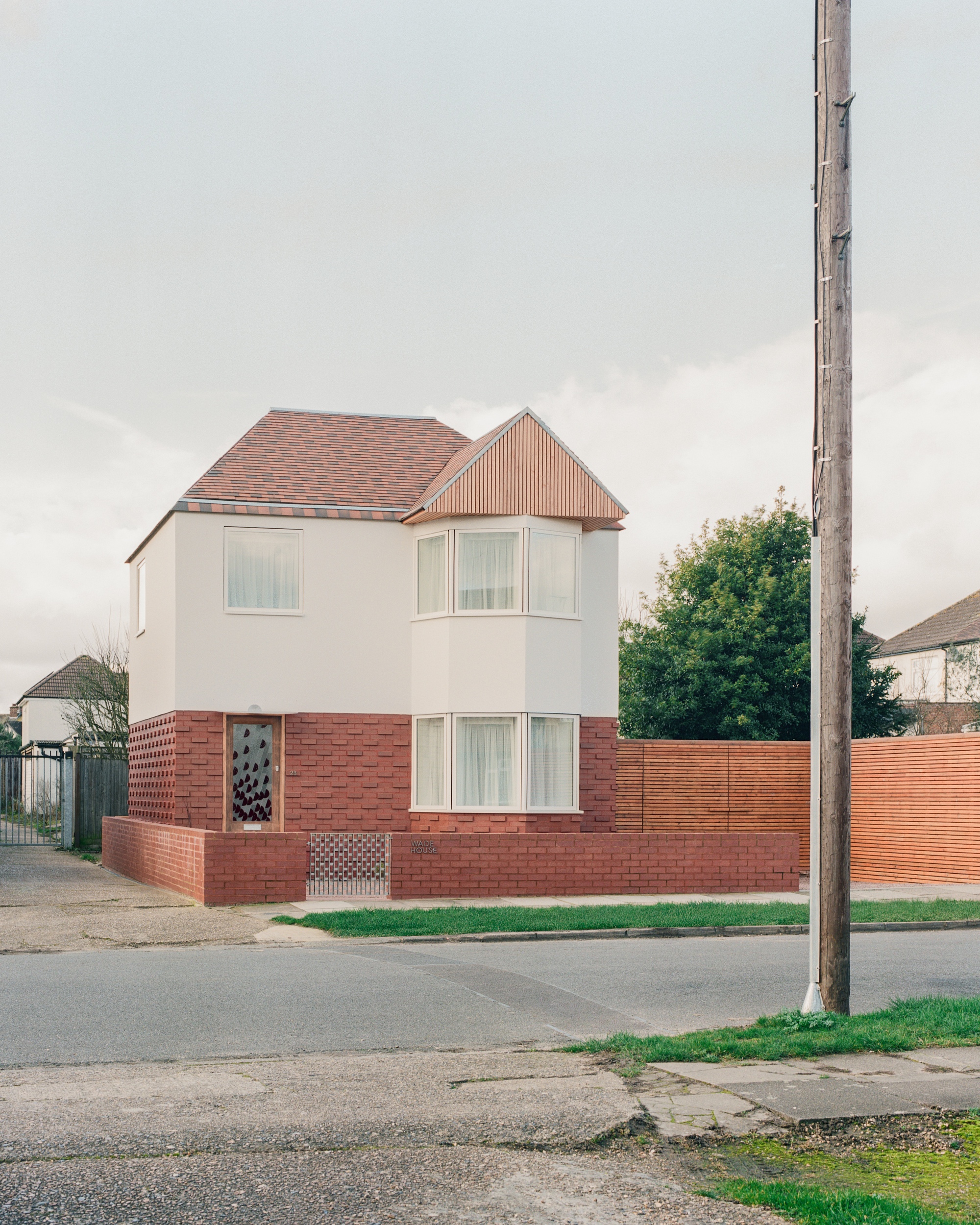 Street view of the brick and render house with timber fence, seen past a utility pole under a cloudy sky