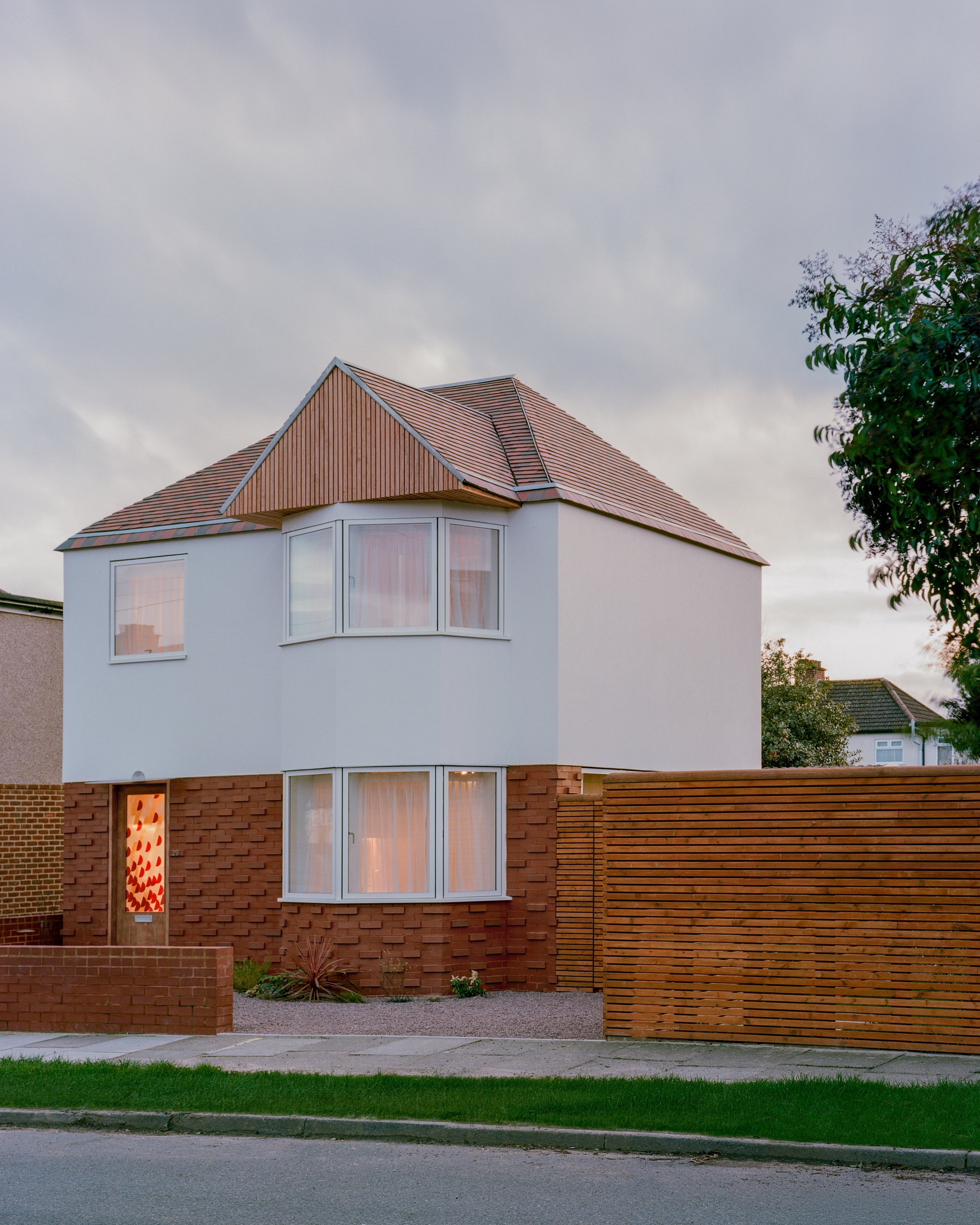 Street facade with bay windows, patterned red brick base and a timber-clad gable, seen under heavy evening clouds