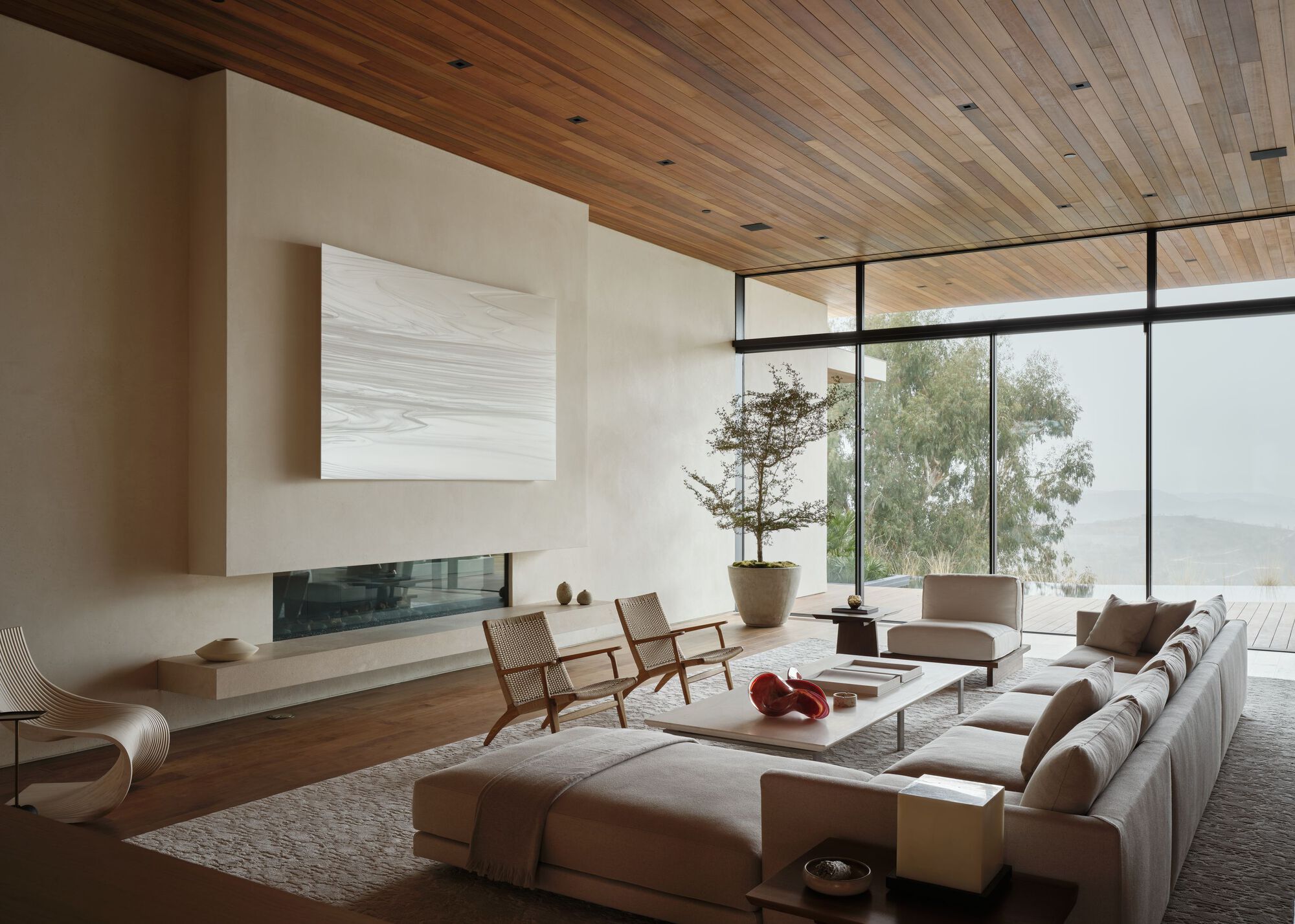 Living room with a wood plank ceiling, linear fireplace and sectional sofa facing floor-to-ceiling glass and misty hills