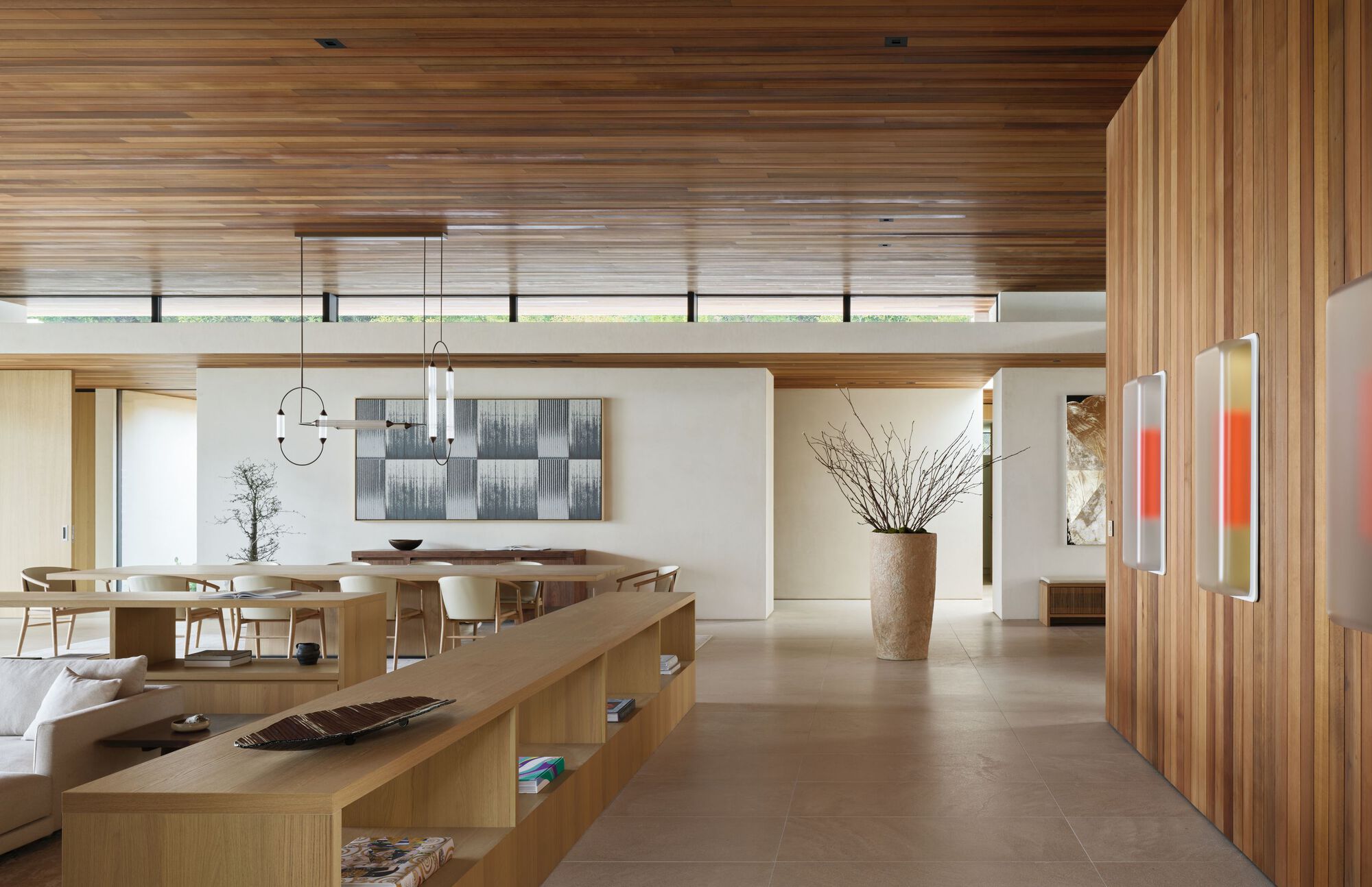 Open living and dining space with a low oak shelving divider, cedar wall panel and timber ceiling in soft daylight