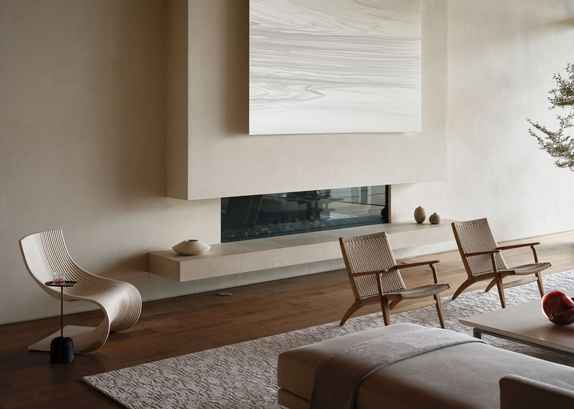 Floating stone hearth with a linear fireplace beneath a pale marbled panel, flanked by woven lounge chairs on a walnut floor