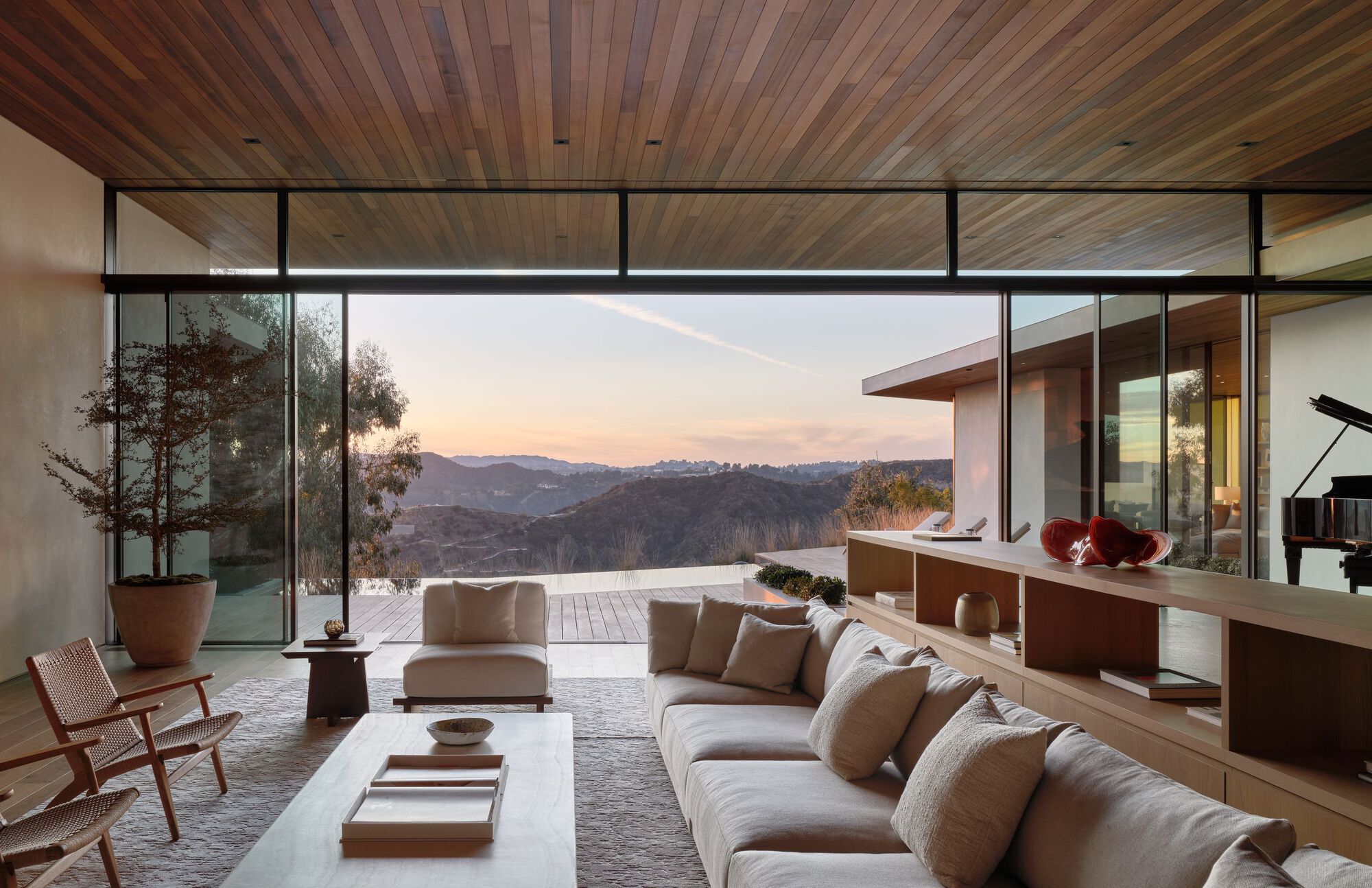 Living room with a long linen sofa and wood ceiling opening through sliding glass to hazy hills at sunset