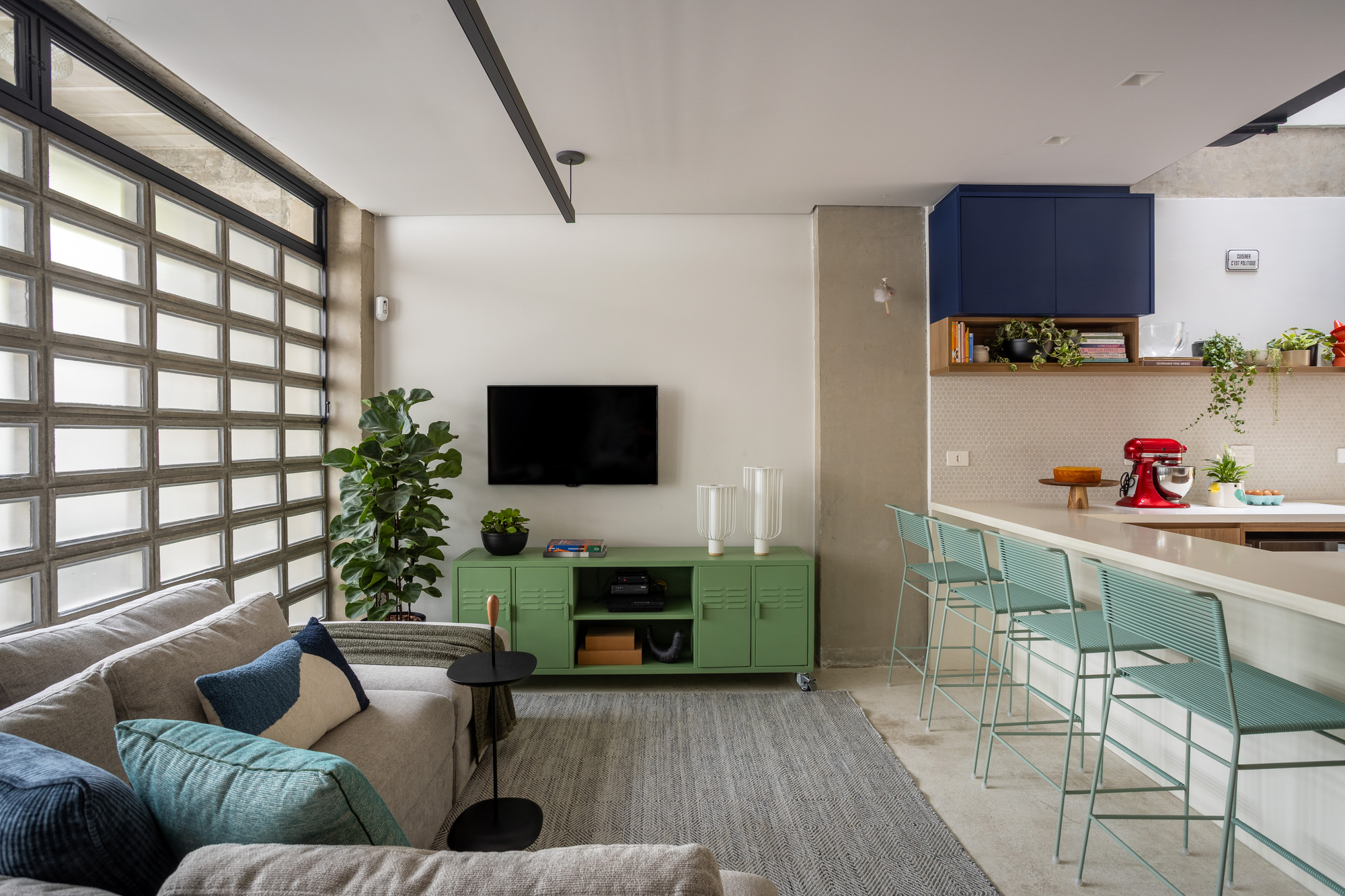 Living area with a glass block window wall, green metal media cabinet and mint bar stools at the kitchen counter