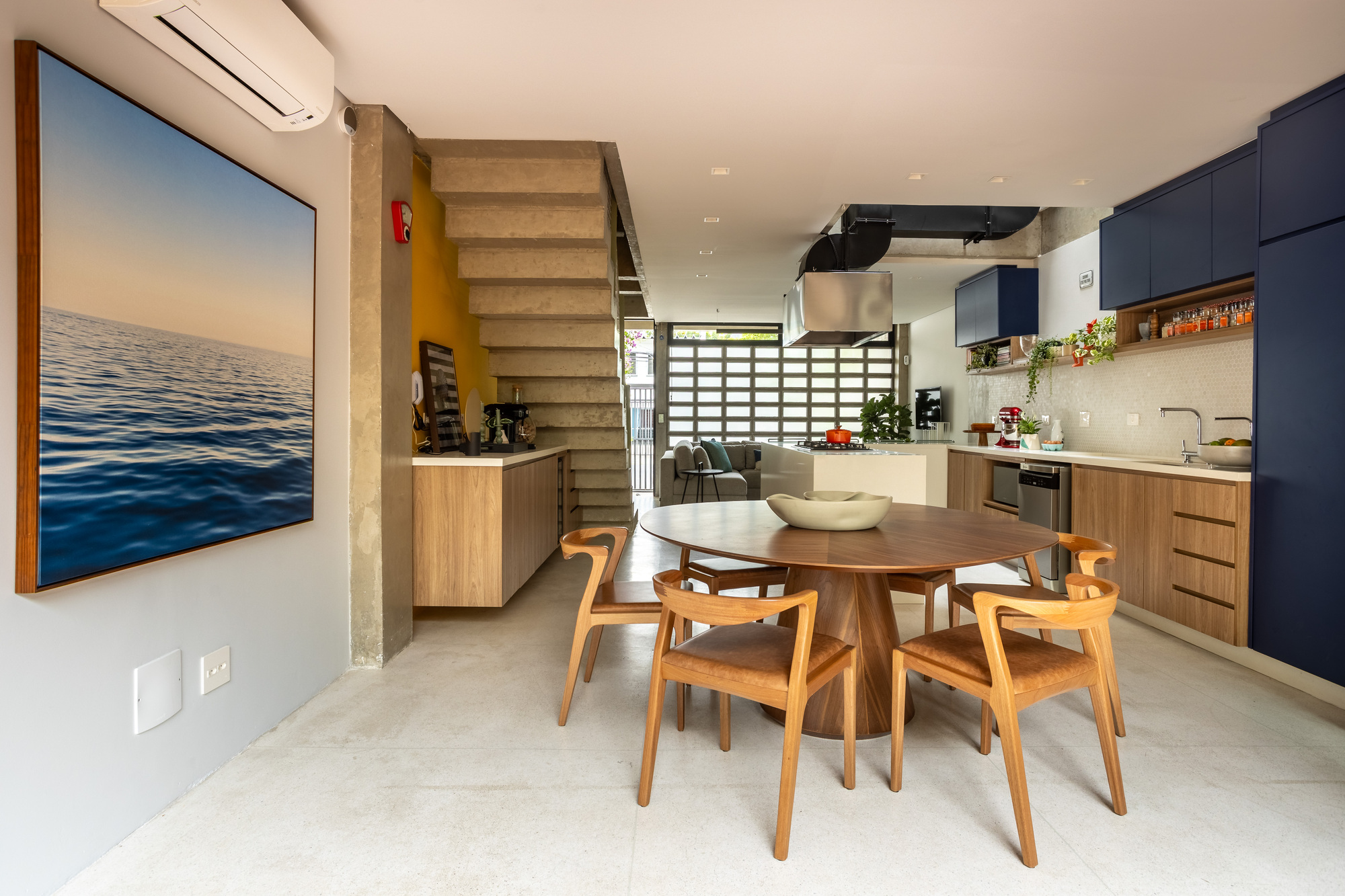 Open dining and kitchen space seen past a large seascape painting, with a stepped concrete stair and glass block wall beyond