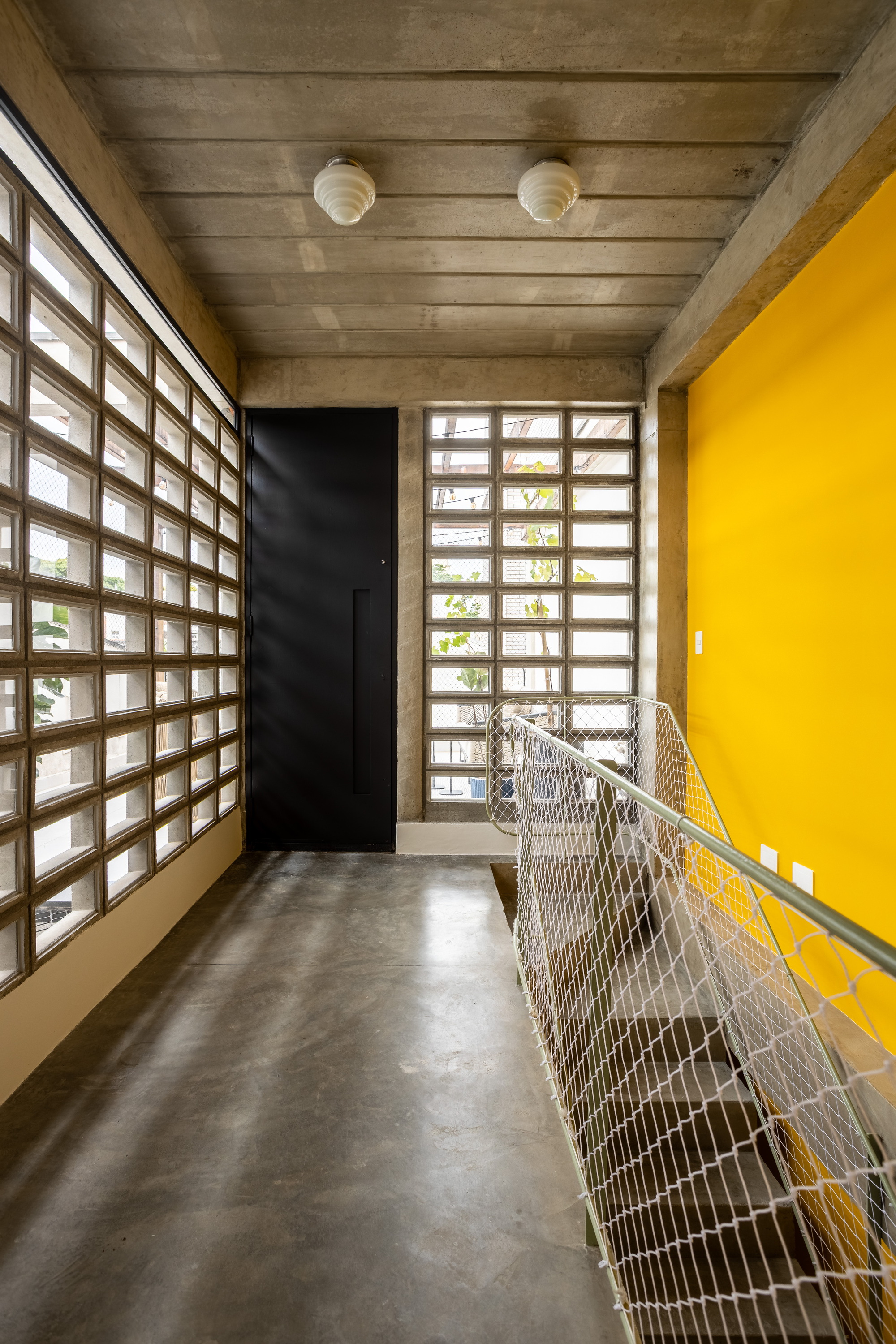 Upper landing with concrete block screen walls, a black pivot door and a yellow wall beside a netted stair guard in daylight
