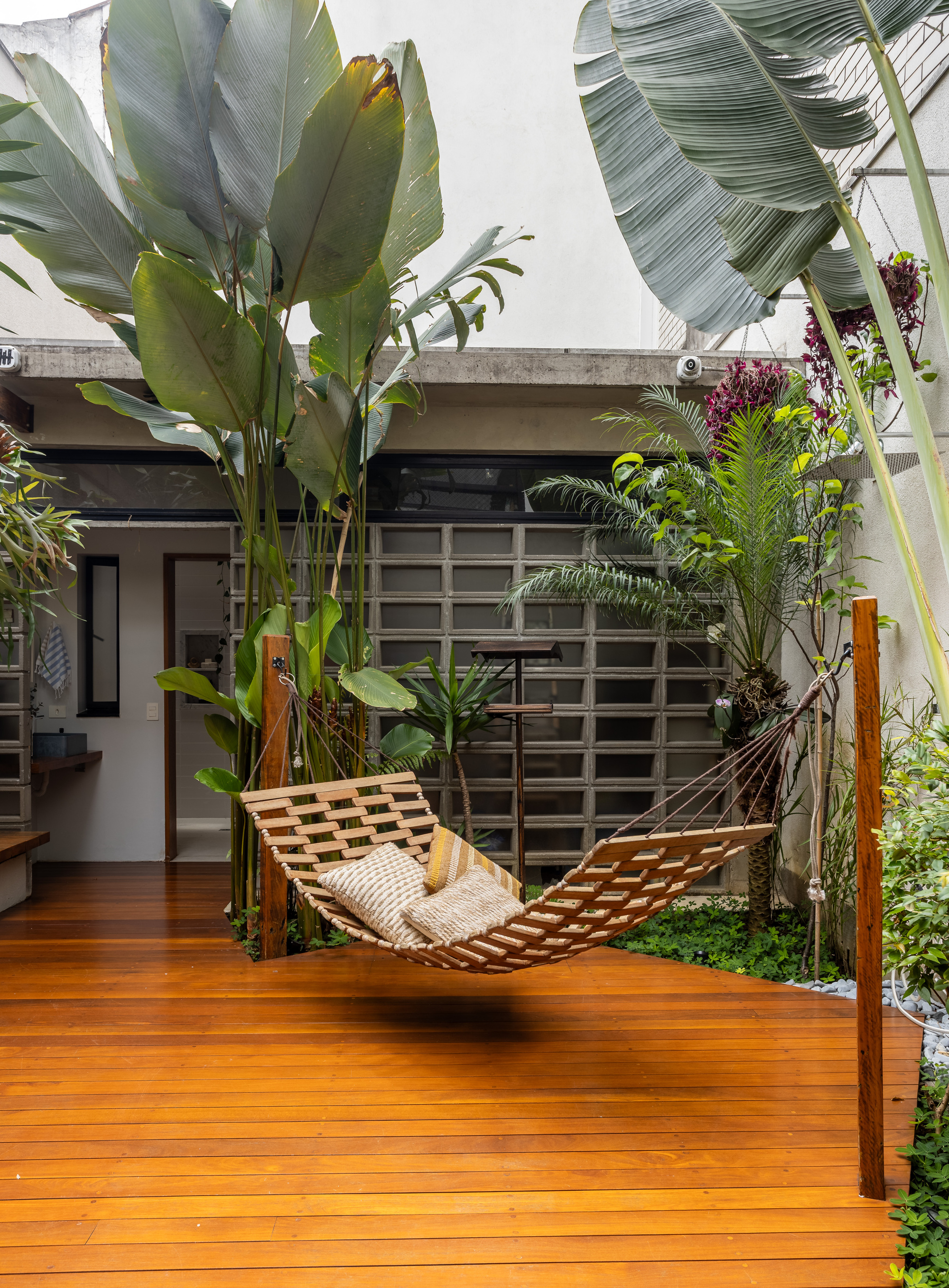 Timber deck courtyard with a slatted hammock, banana leaves and palms in front of a concrete block screen