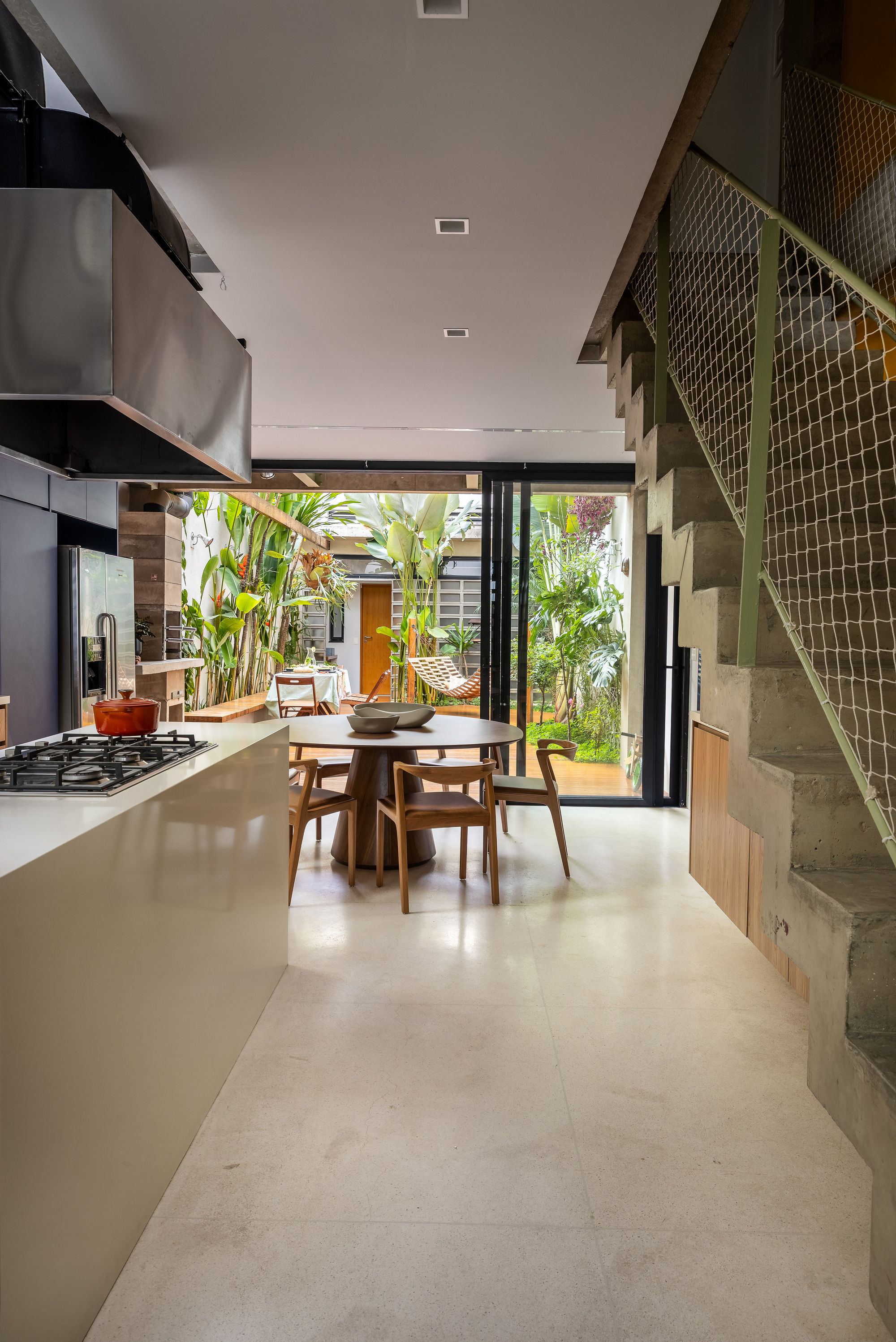 Kitchen island and round dining table facing a sliding glass wall that opens onto a planted courtyard, with a concrete stair at right