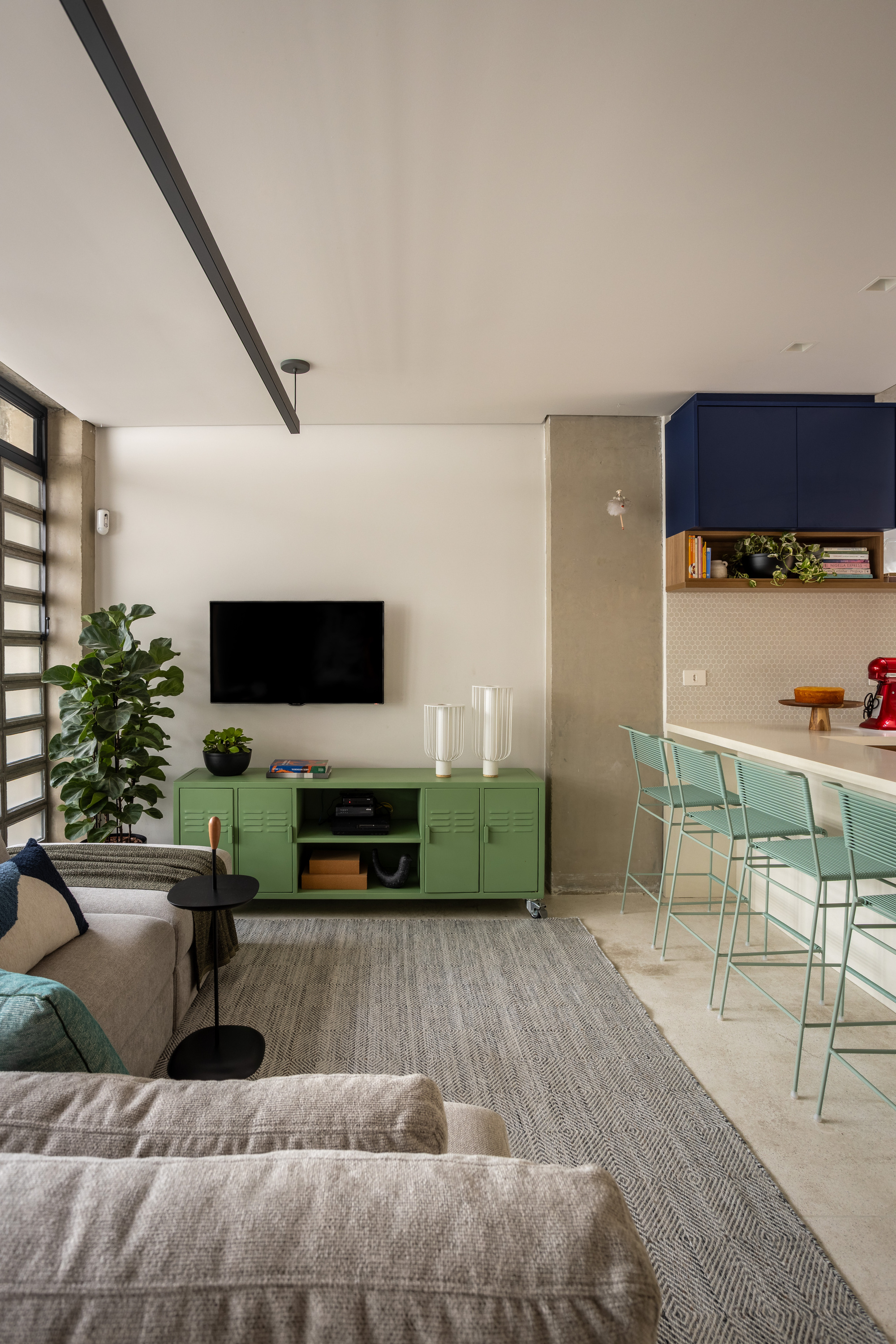 Living area with green metal media cabinet, fiddle-leaf fig and striped rug, with stools lined along the kitchen counter