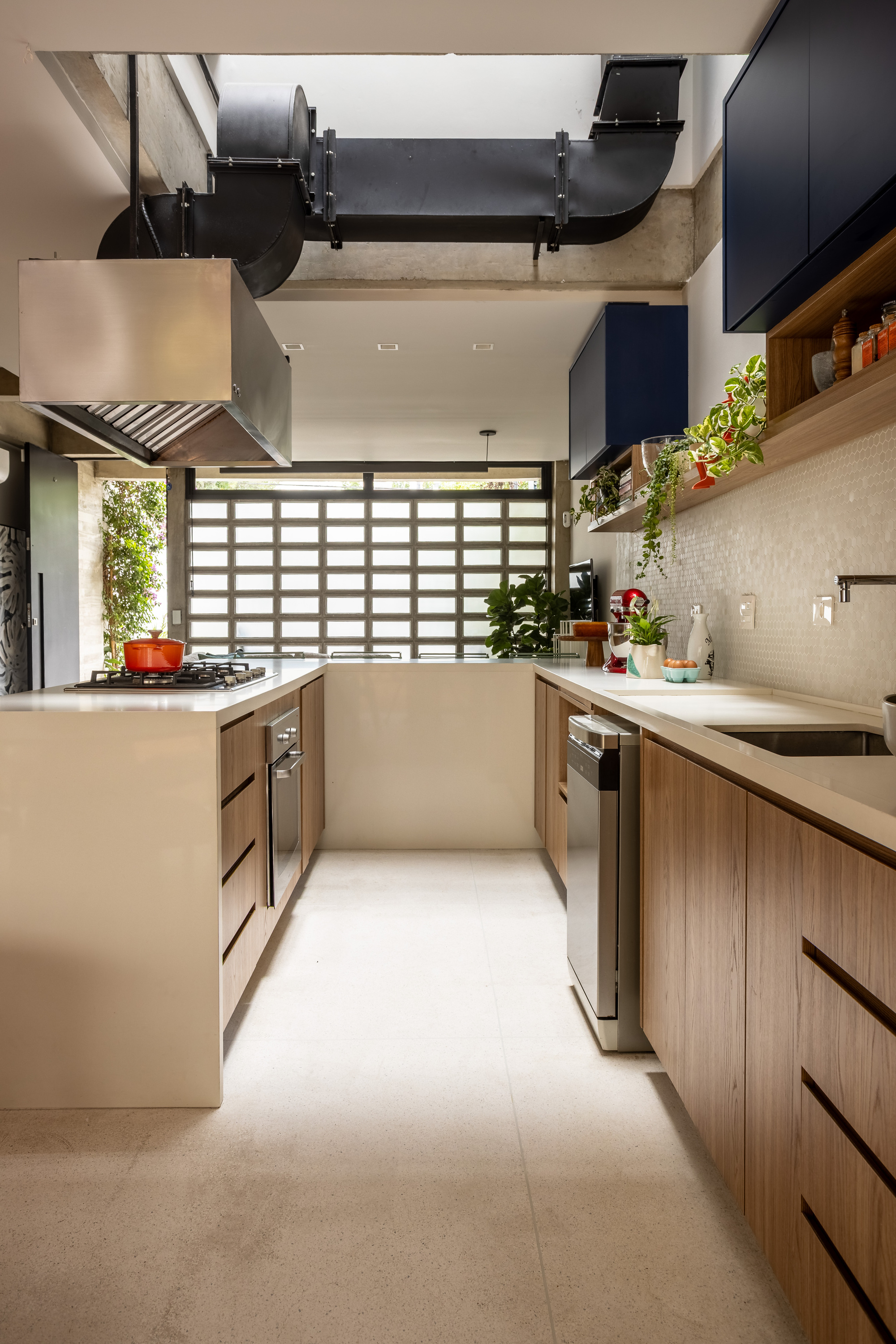 Galley kitchen with timber cabinets, steel hood and exposed black ductwork, ending in a window of concrete block lattice