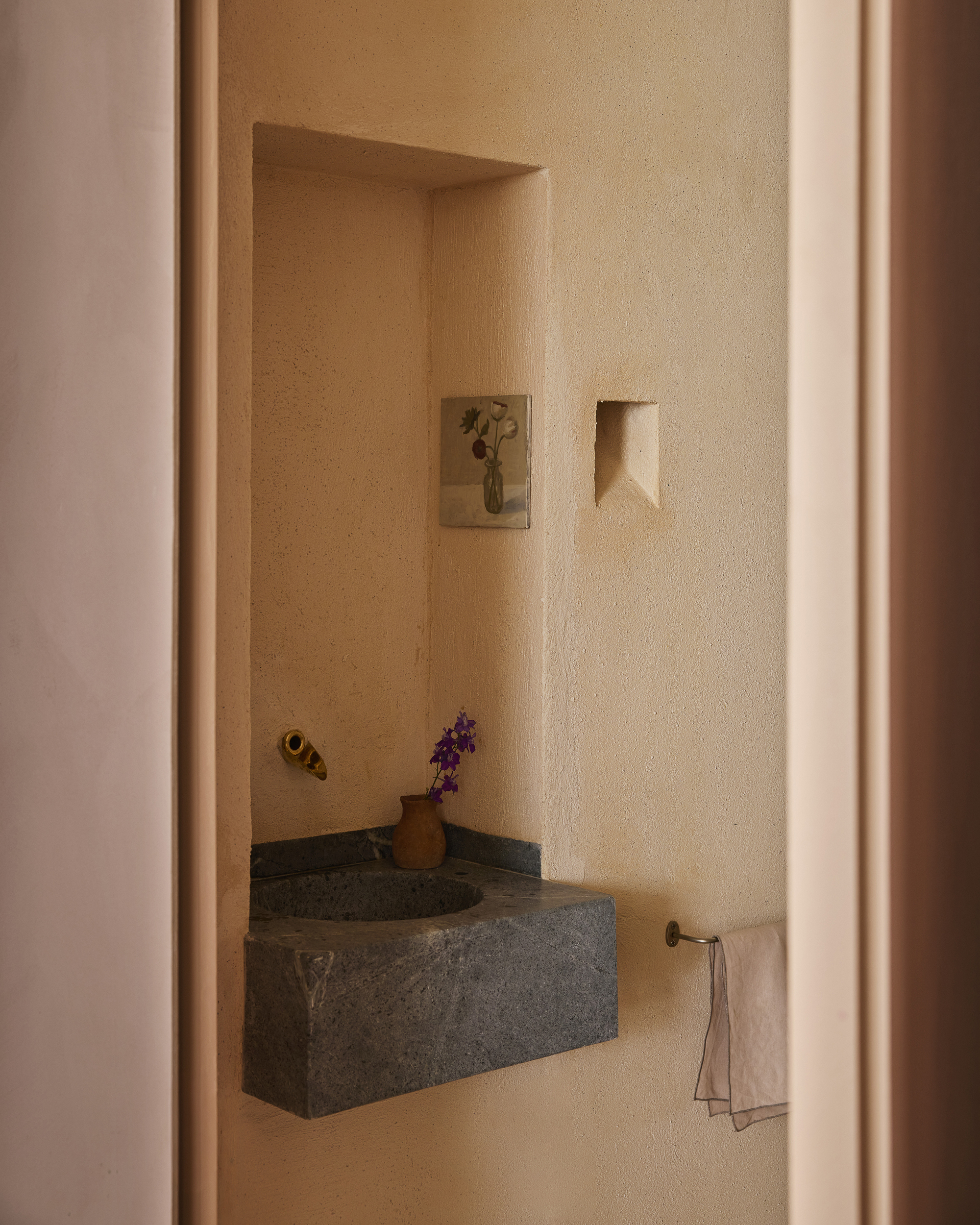 Corner stone basin set in a plastered niche with brass tap, small painting and a vase of purple flowers