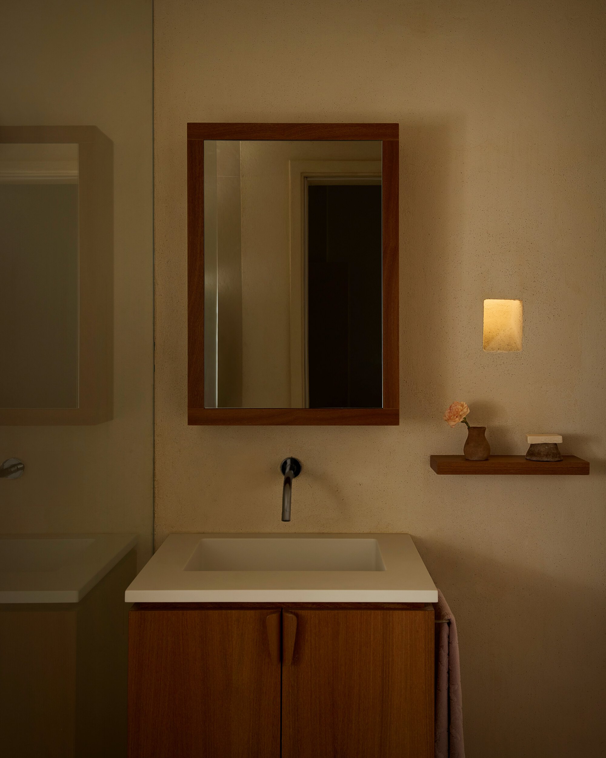 Bathroom vanity with a wood-framed mirror, wall-mounted tap and small alabaster sconce glowing in dim evening light