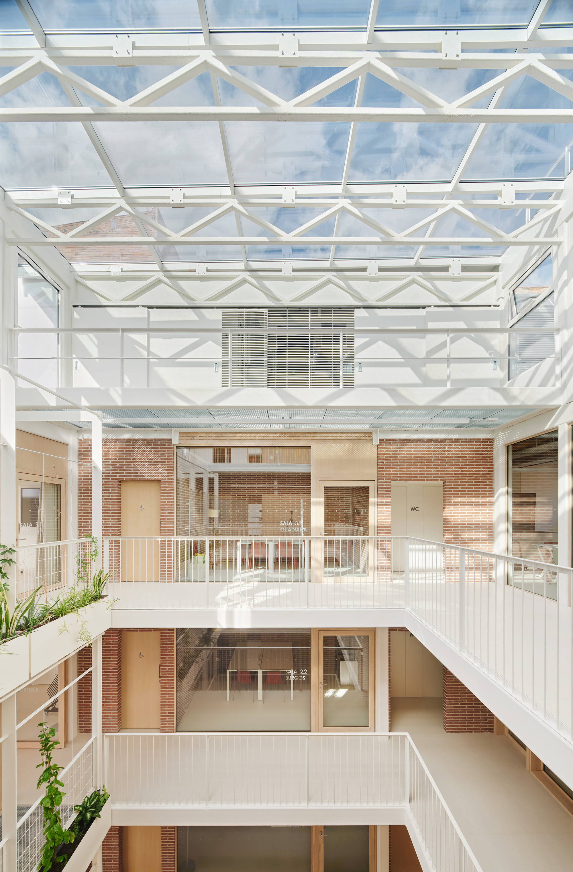 Looking up the atrium to the white steel truss skylight, with brick walls and timber doors on each landing in daylight