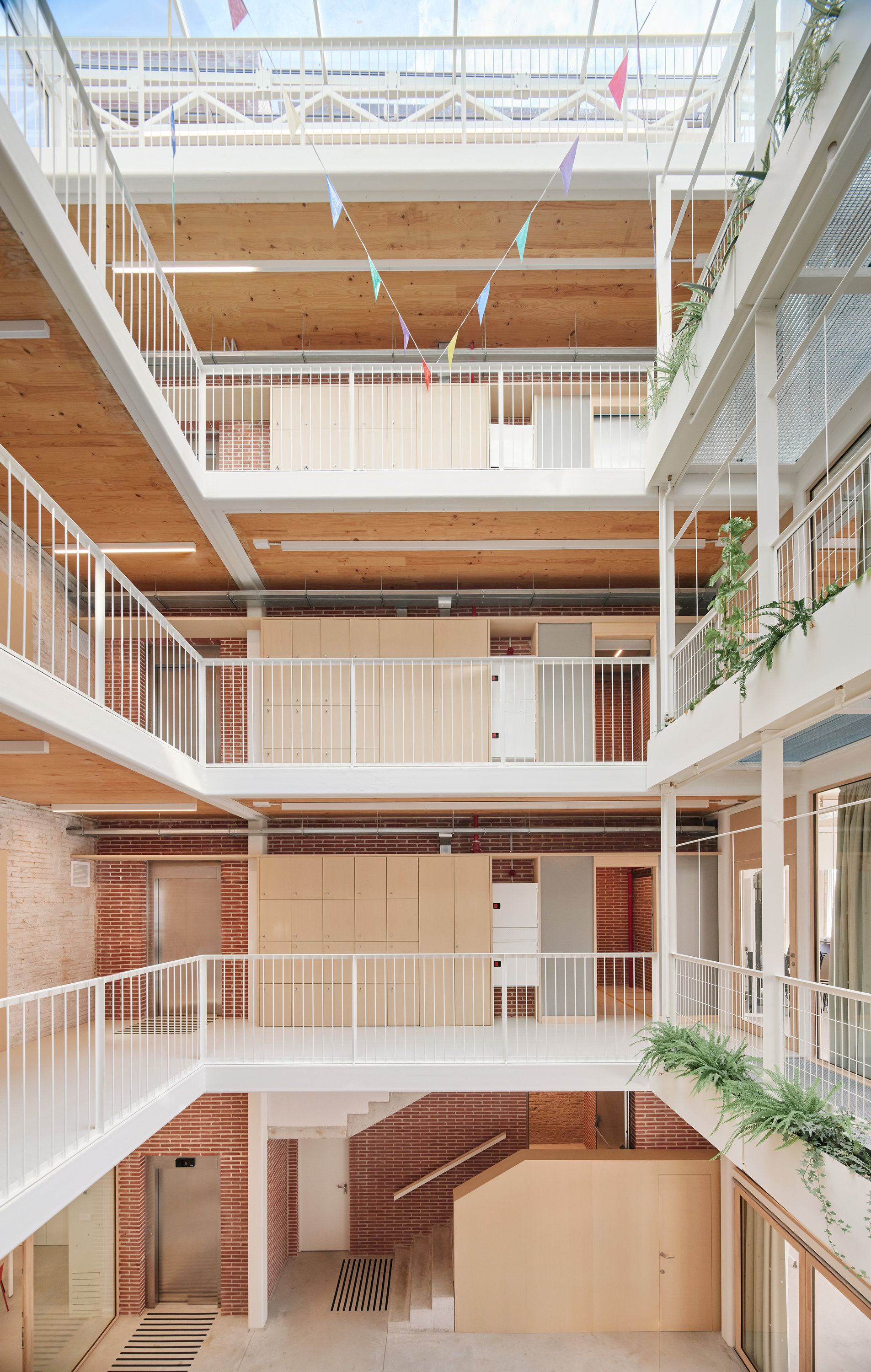 Atrium looking up past white railed walkways, brick walls and timber cabinets to a glazed roof strung with colored bunting