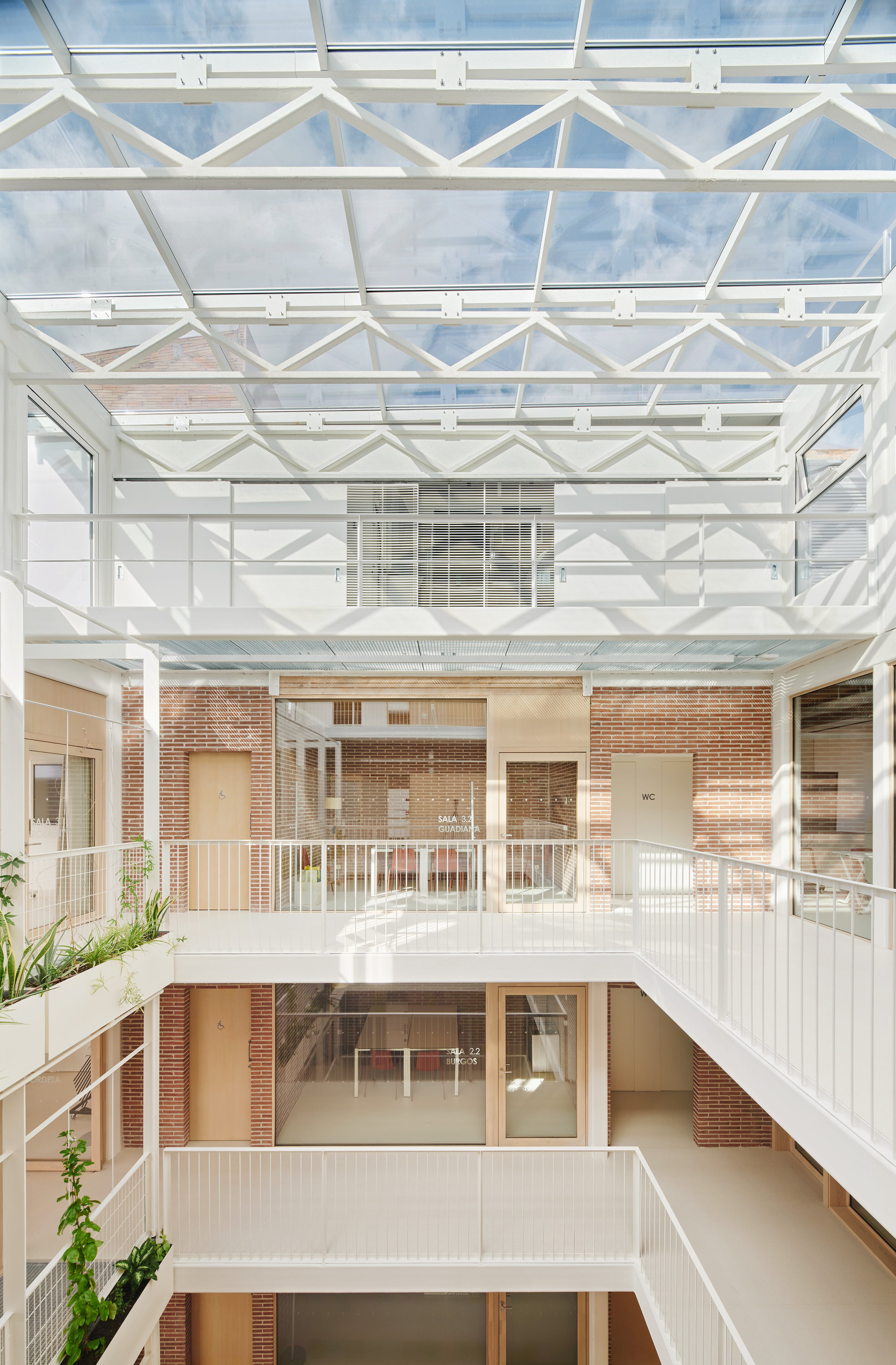 Atrium looking up past white balustraded walkways and brick walls to a steel-framed glass roof under blue sky