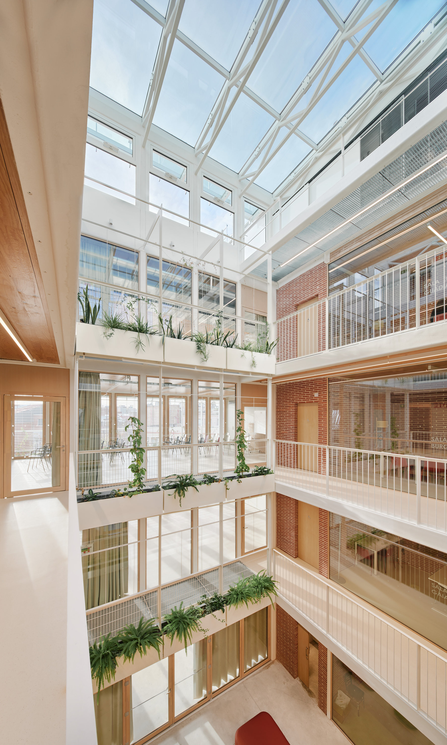 Multi-storey atrium with planters along each balcony edge, brick walls and a glazed roof lit by daylight