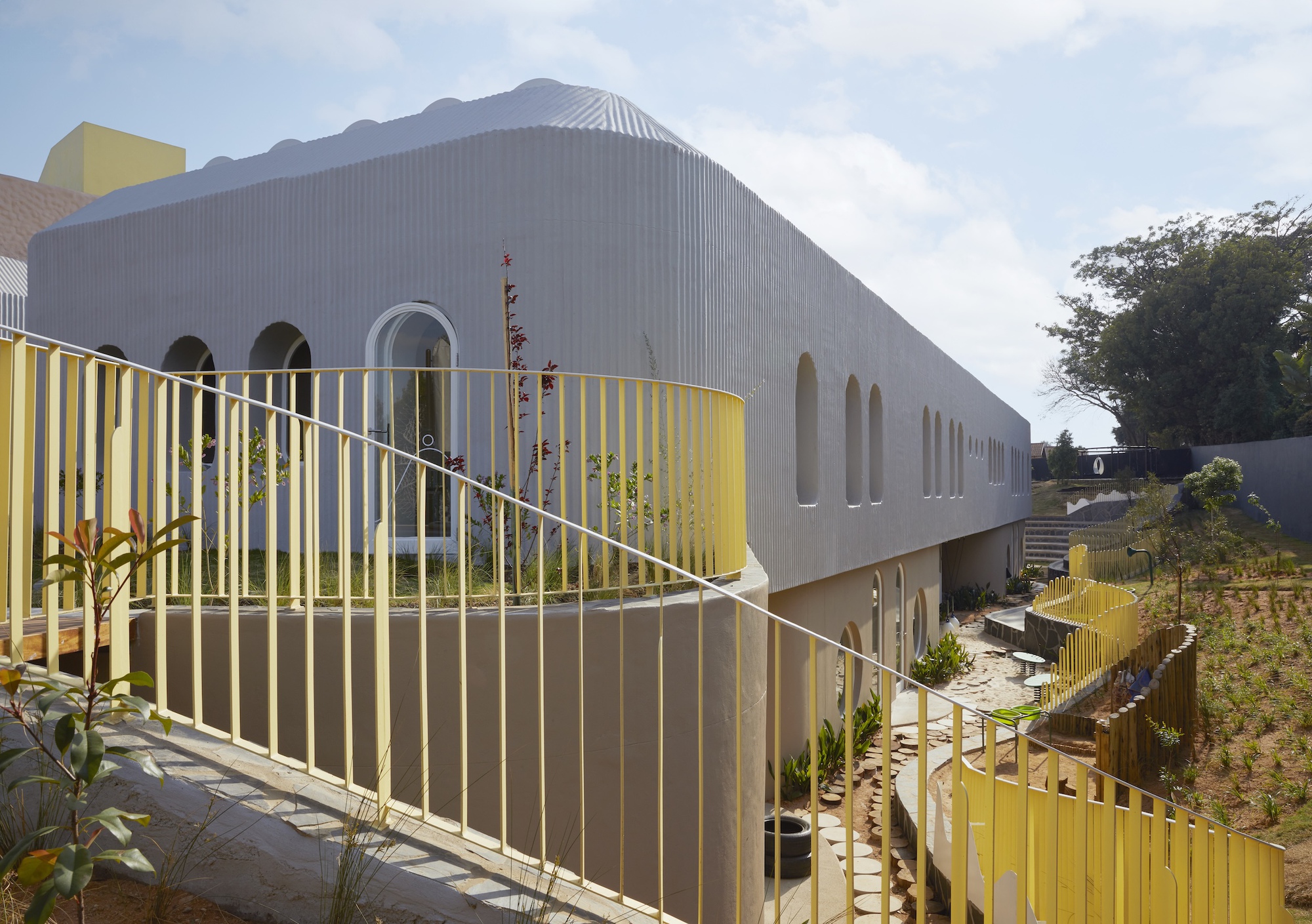Curving yellow balustrade in front of a grey ribbed building with arched windows, set against a hazy blue sky