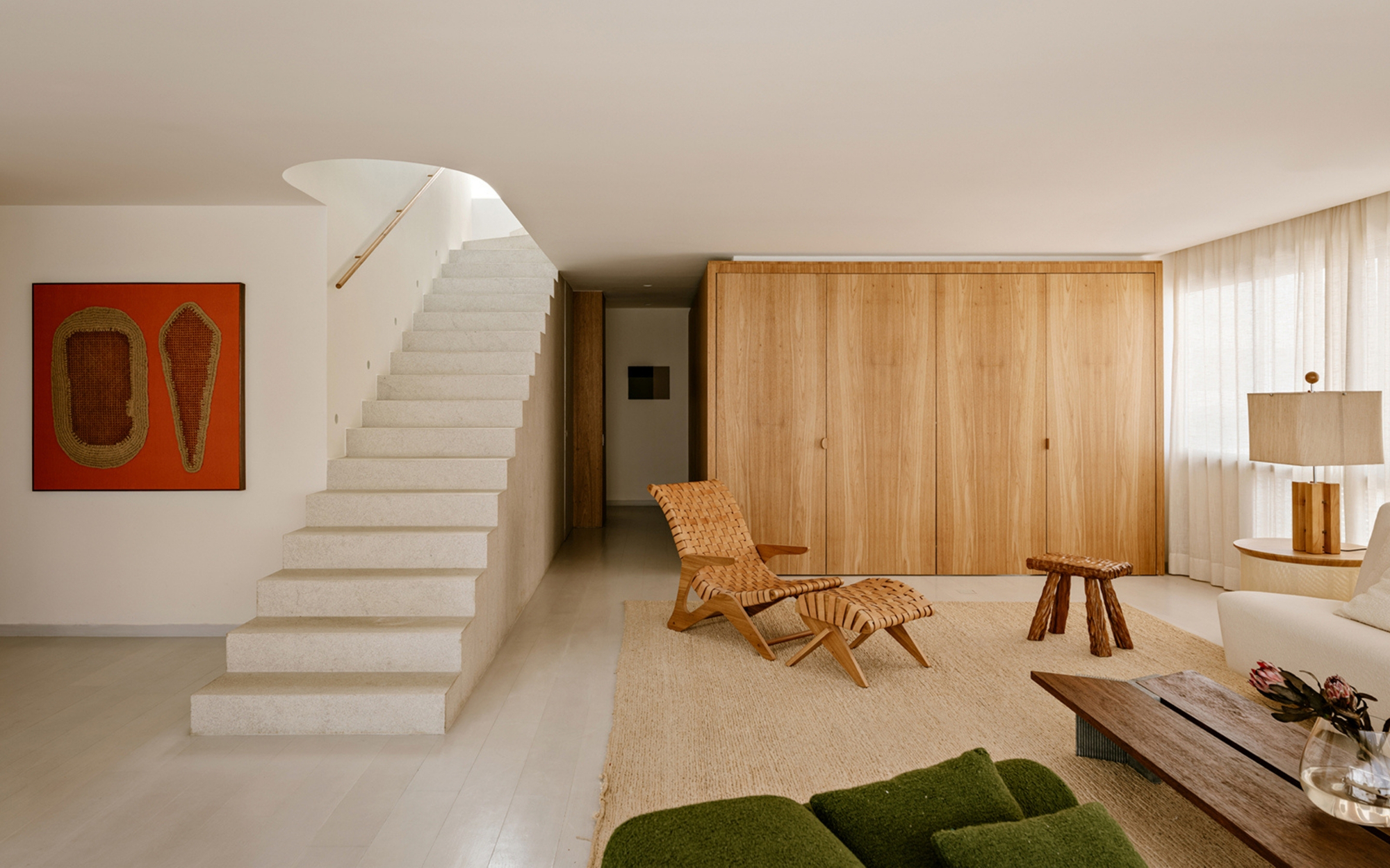 Stone staircase rising beside a wall of oak cabinet doors, with a woven lounge chair on a jute rug in soft daylight