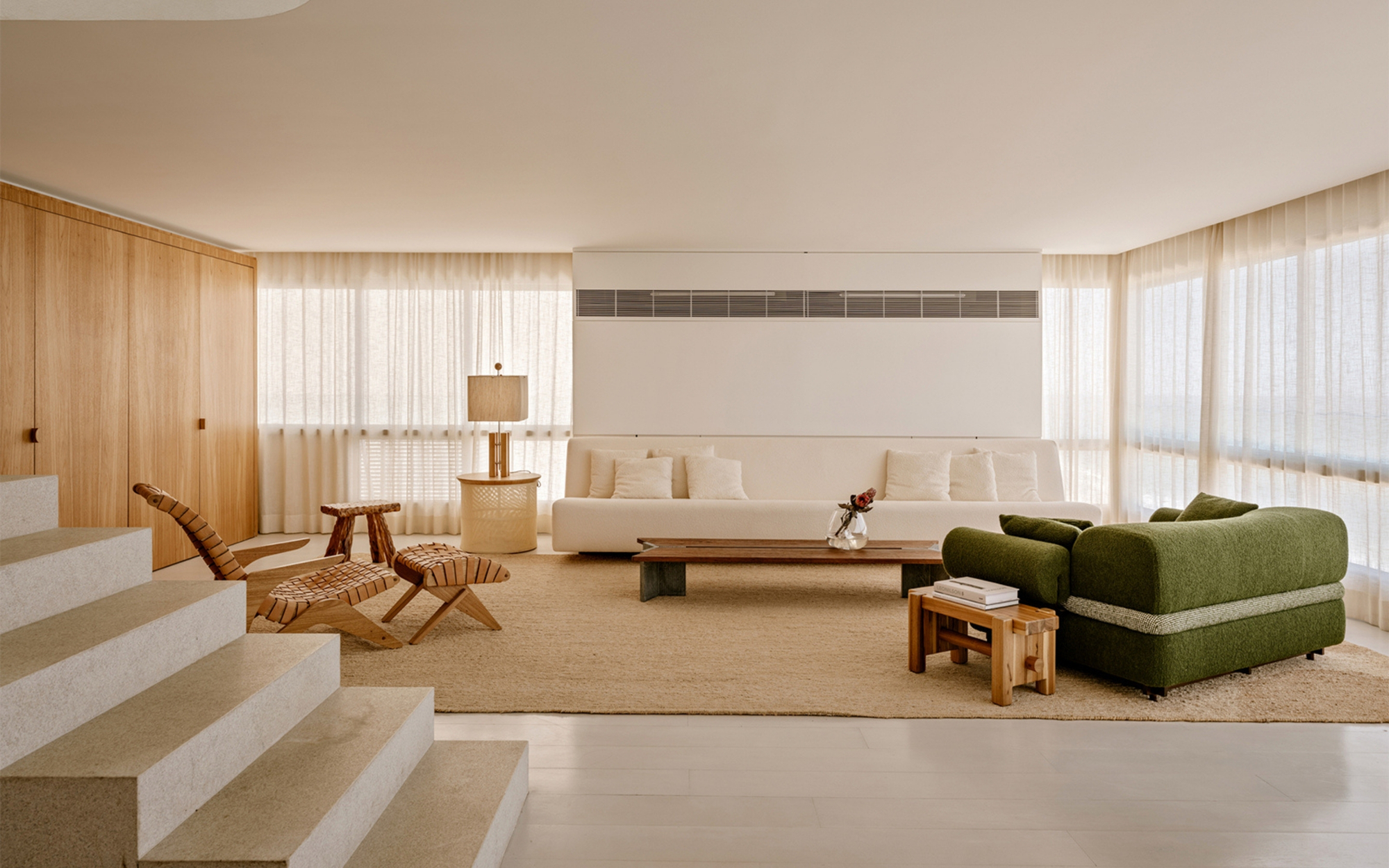 Living room with a white sofa, low timber table and green bouclé seat, backed by sheer curtains glowing with daylight