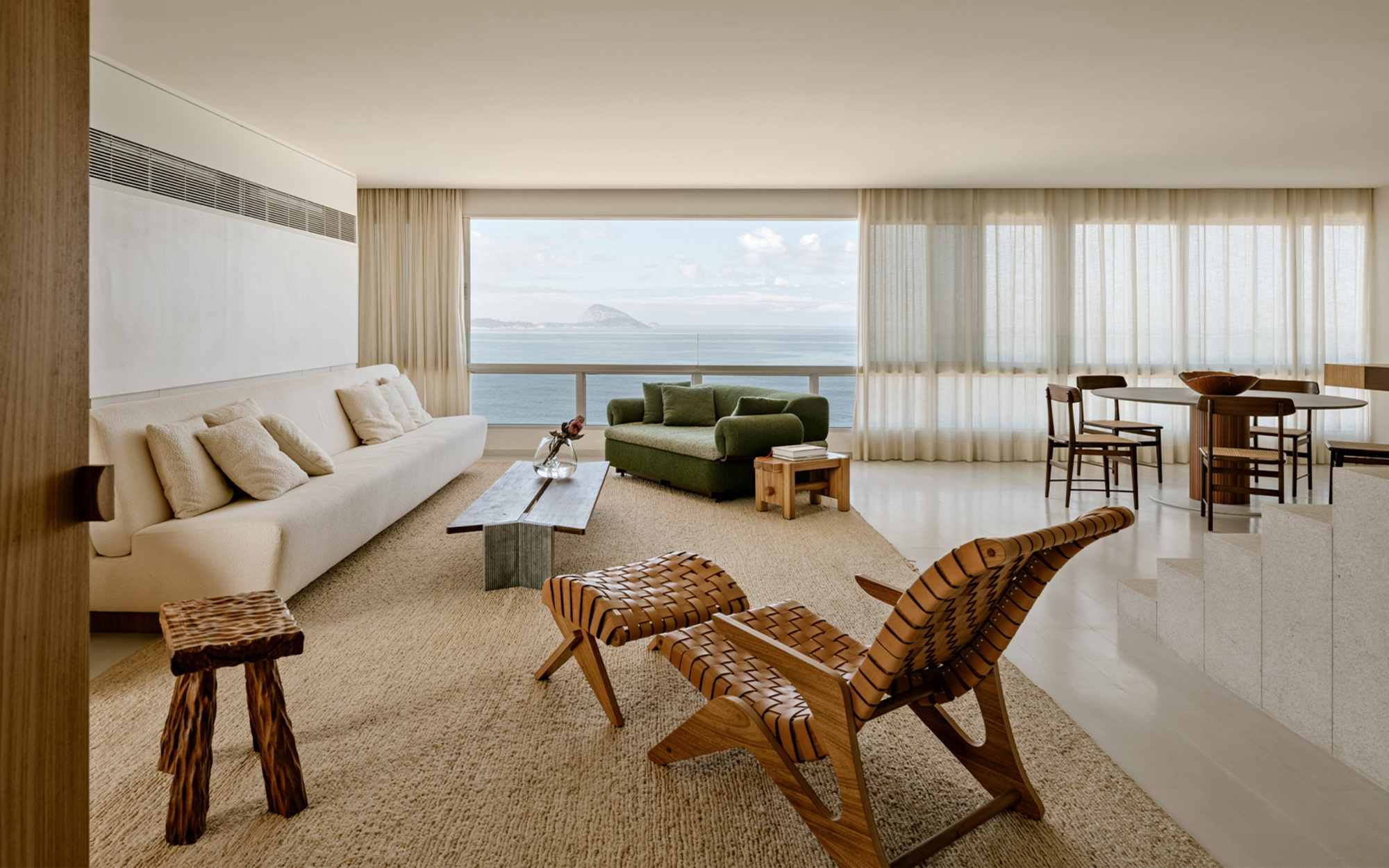 Living room with a cream sofa, woven lounge chair and green armchair facing a sea view under a partly cloudy sky