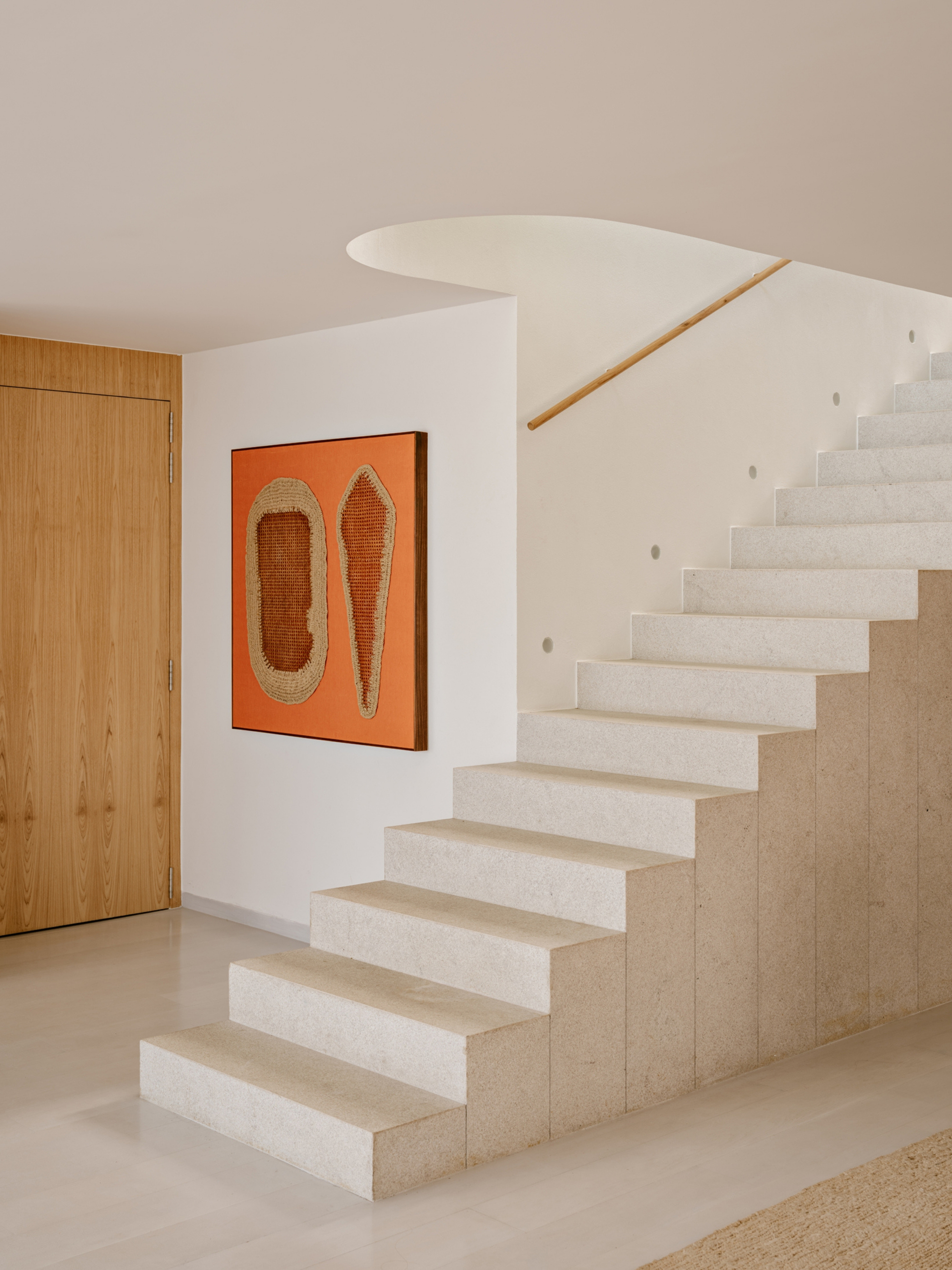 Limestone block stair beside an orange woven artwork and an oak door, with a curved white soffit above in soft light