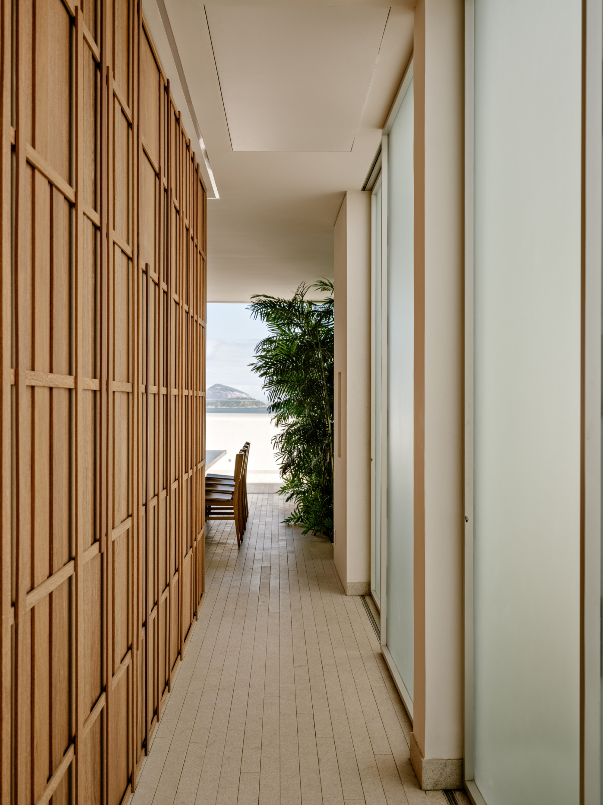Covered walkway lined with a timber lattice screen and frosted glass doors, opening to a palm and distant hill