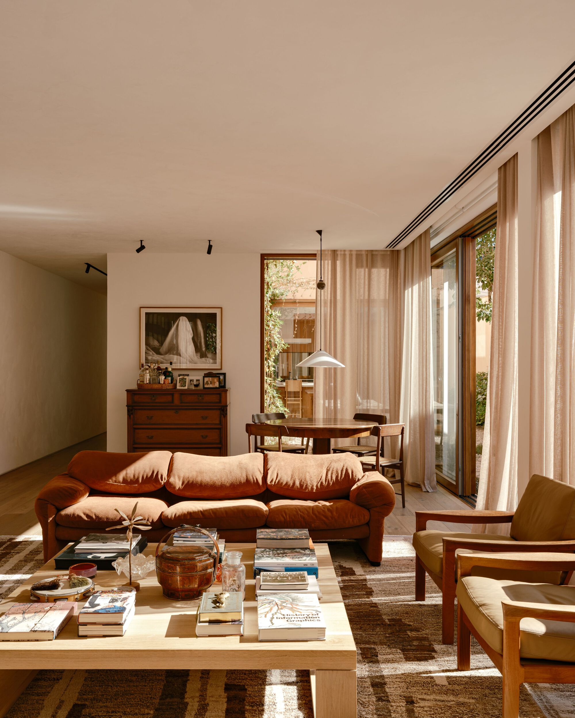 Living room with a rust-colored sofa, low timber coffee table and sheer curtains filtering afternoon light from the garden