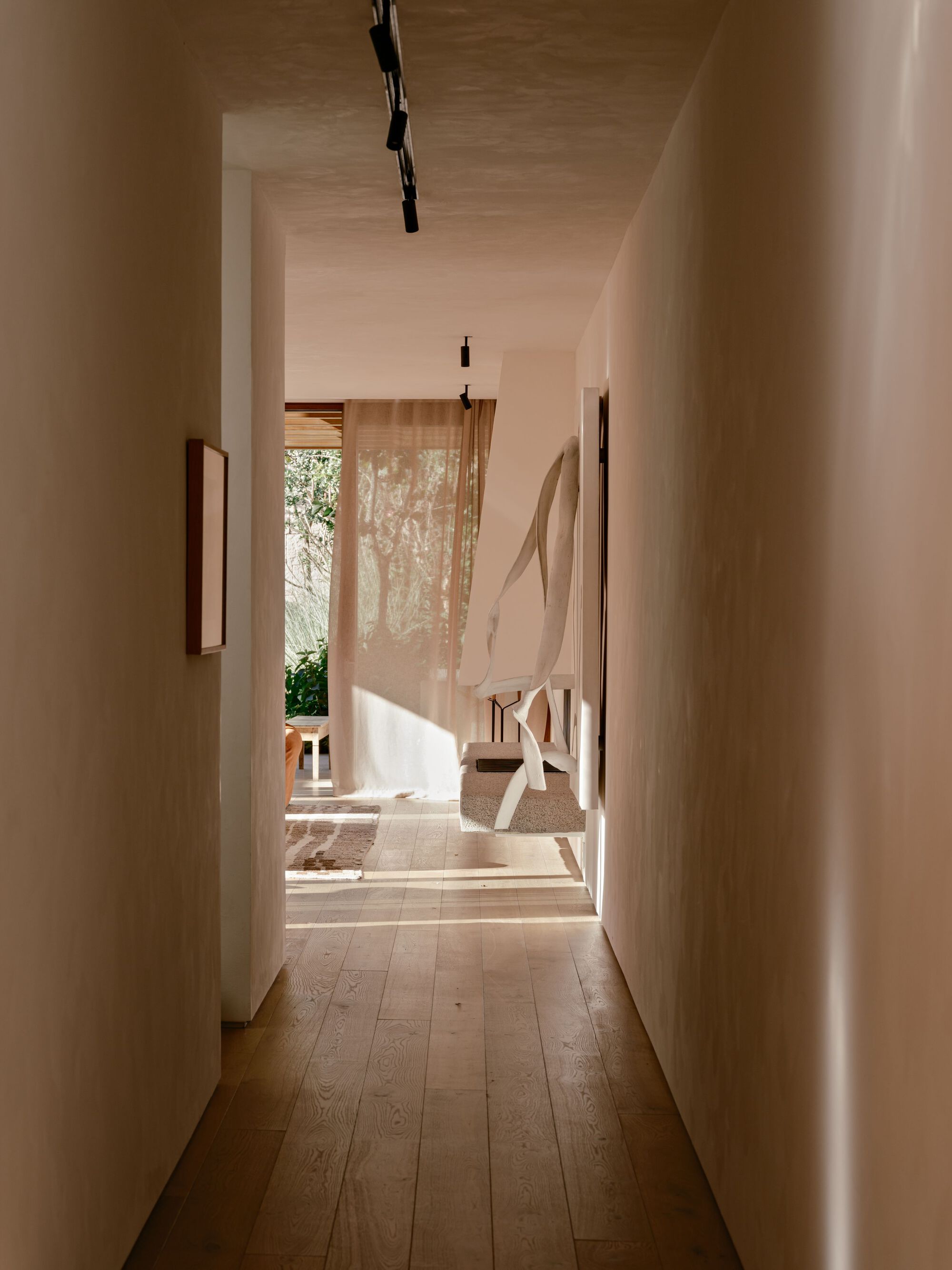 Plaster-walled hallway with wide oak floorboards leading to a sheer curtain, with afternoon sun streaking across the floor