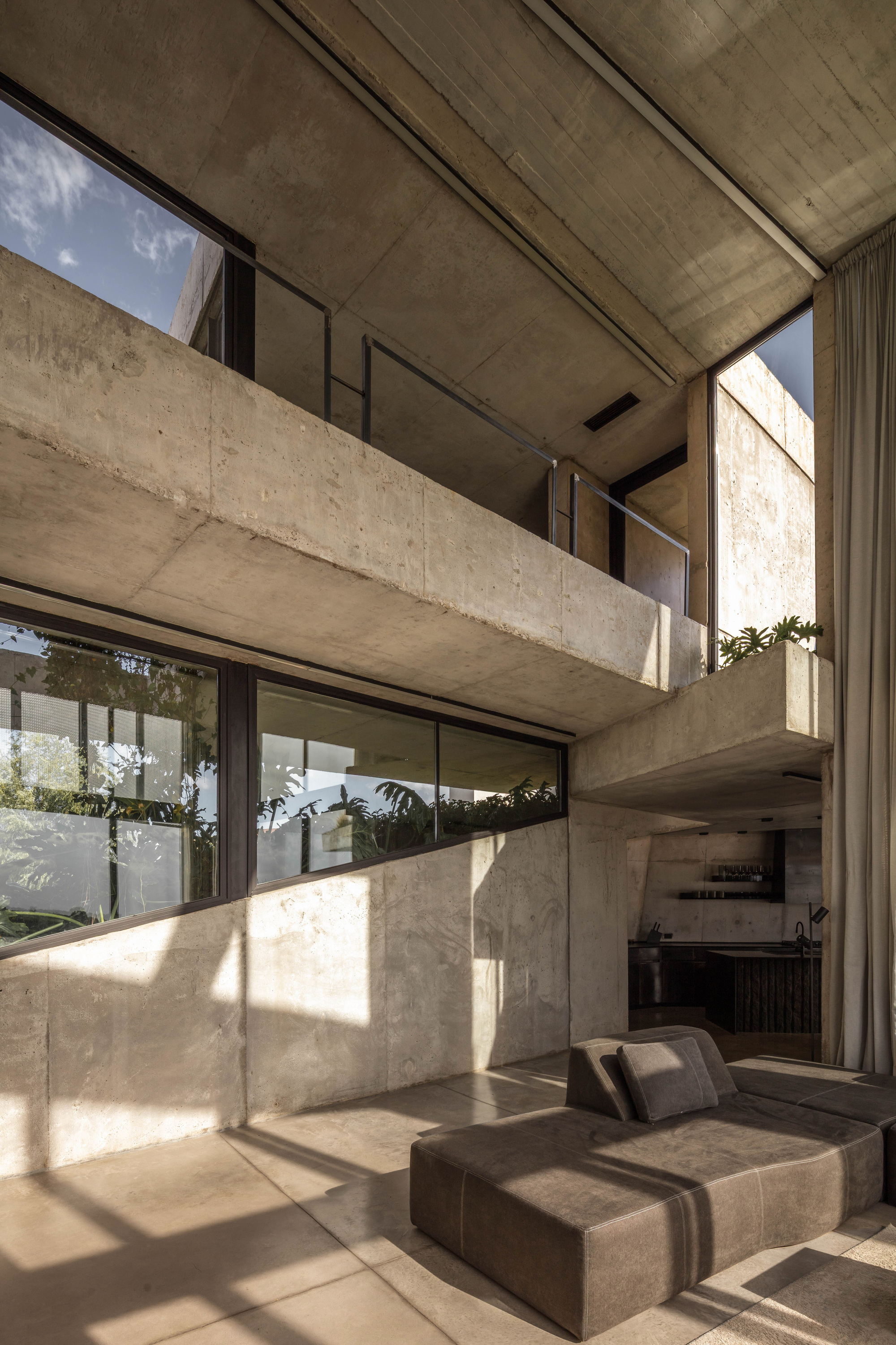 Interior of raw concrete balconies and sloped wall above a low leather sofa, with sunlight casting window shadows across the floor