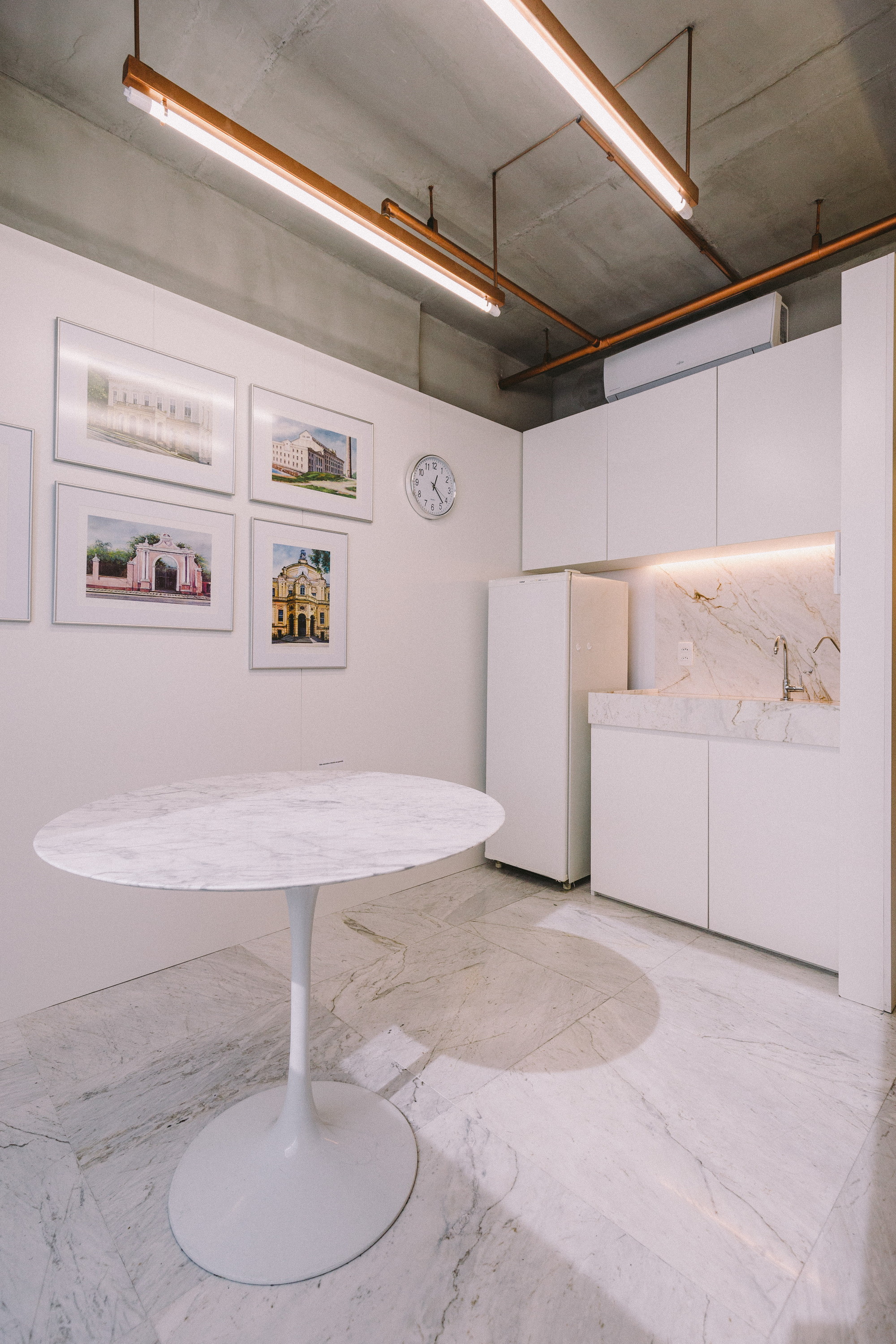 Small kitchenette with a round marble table, framed building photographs on the wall and a marble backsplash lit from below