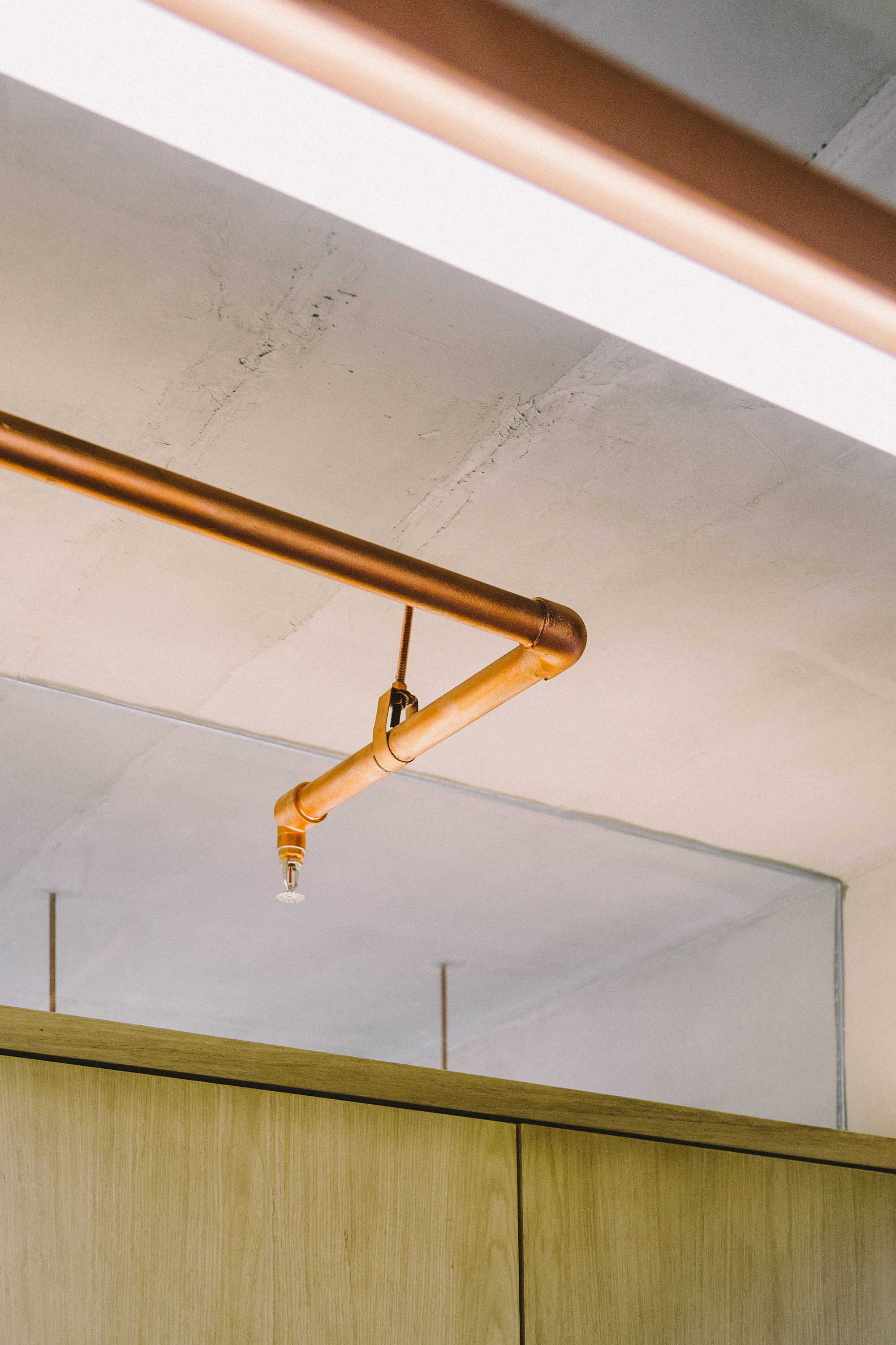 Copper sprinkler pipe with a bent elbow running beneath a concrete ceiling above oak cabinet doors and a glass panel