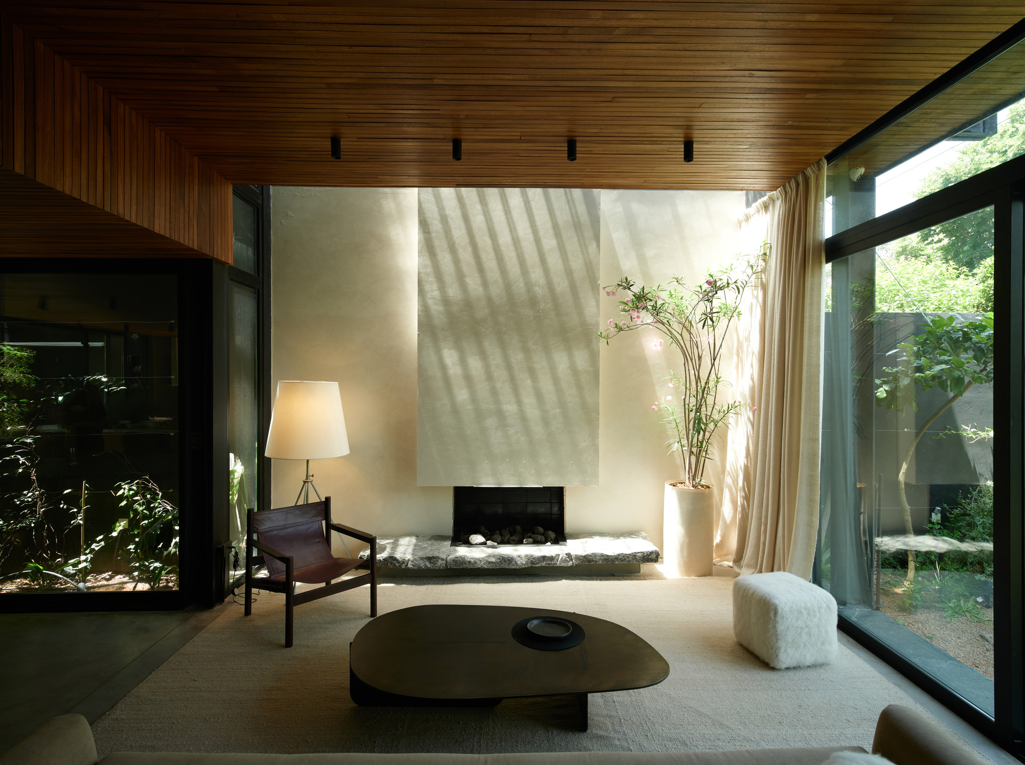Living room with a plaster fireplace wall, stone hearth and slatted timber ceiling, sunlight casting diagonal shadows