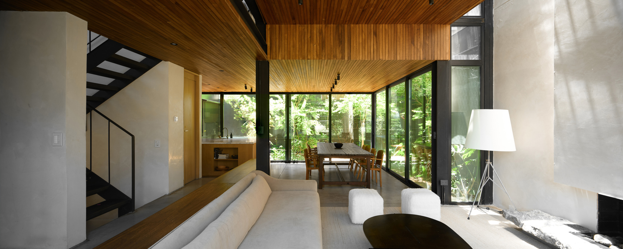 Wide interior view from sofa to dining table, with a black steel stair on the left and garden glazing beyond