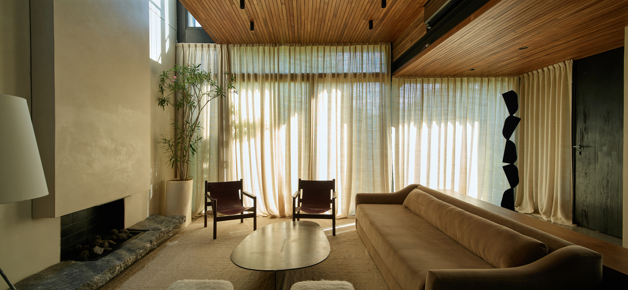 Wide view of the living room with two leather chairs, oval coffee table and sheer curtains filtering afternoon light