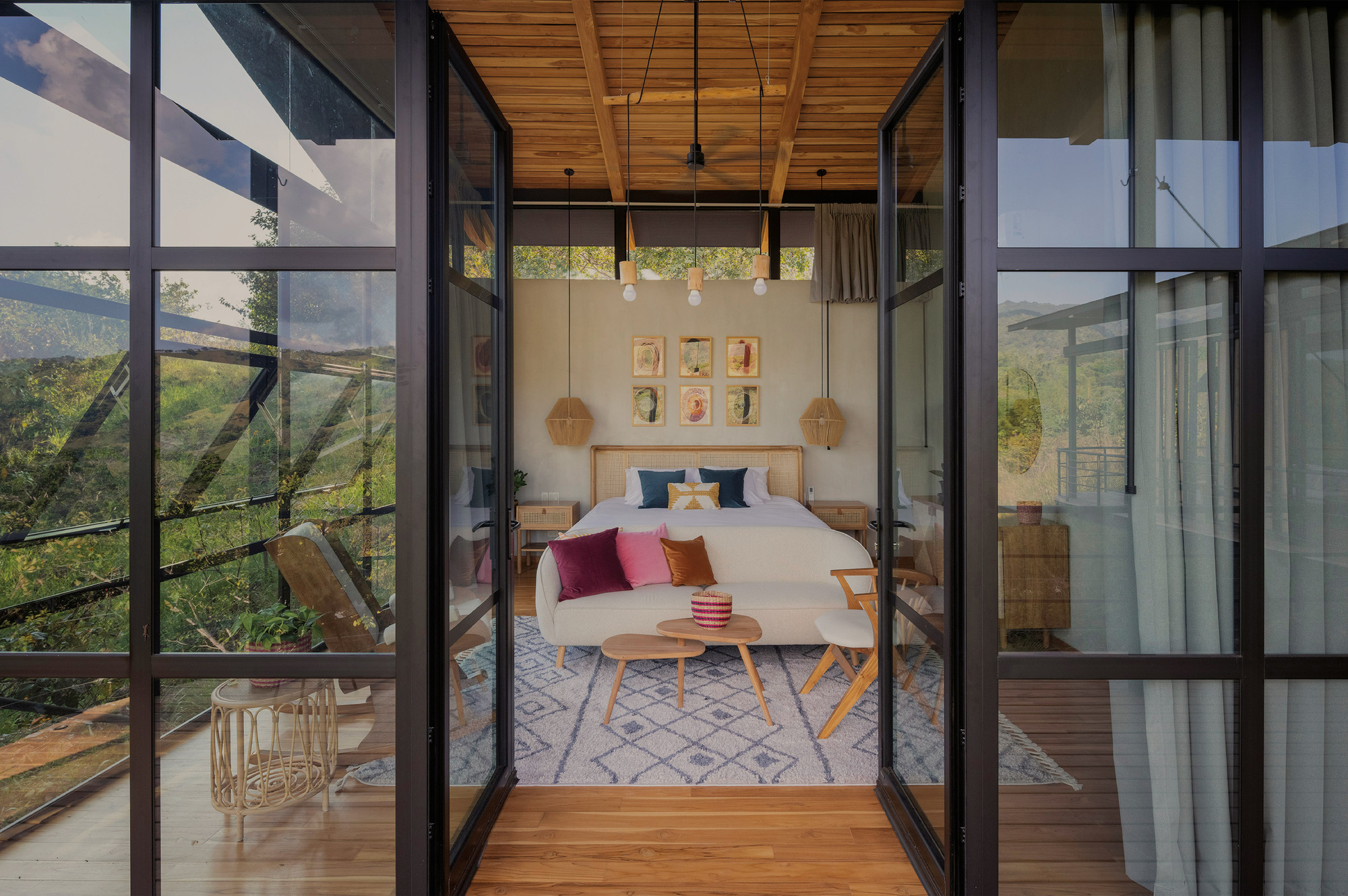 Open black-framed glass doors leading to a bedroom with timber ceiling, rattan pendants and a patterned rug