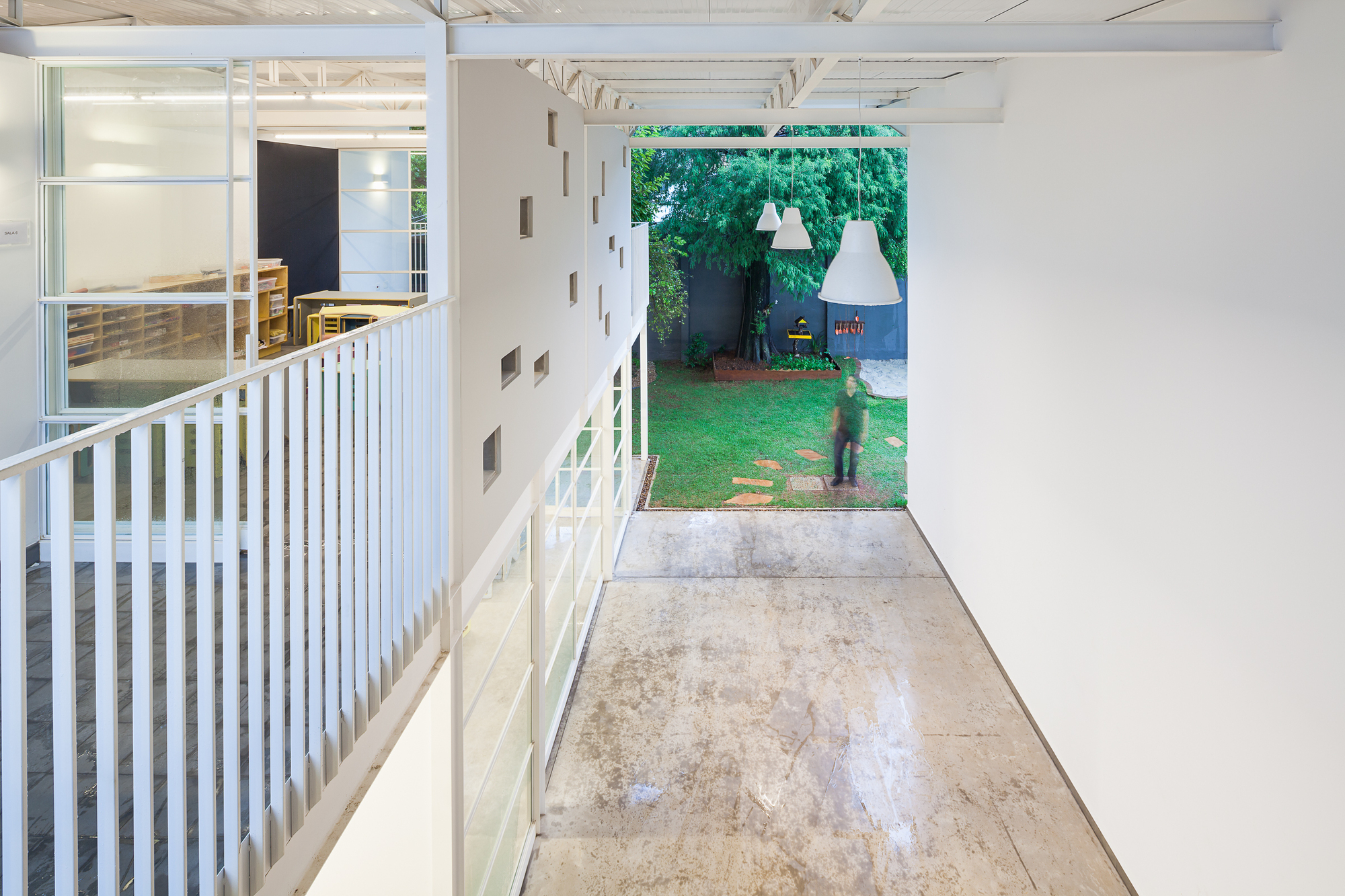 View from the upper walkway along a white balustrade to a polished concrete floor, with a person standing in the garden