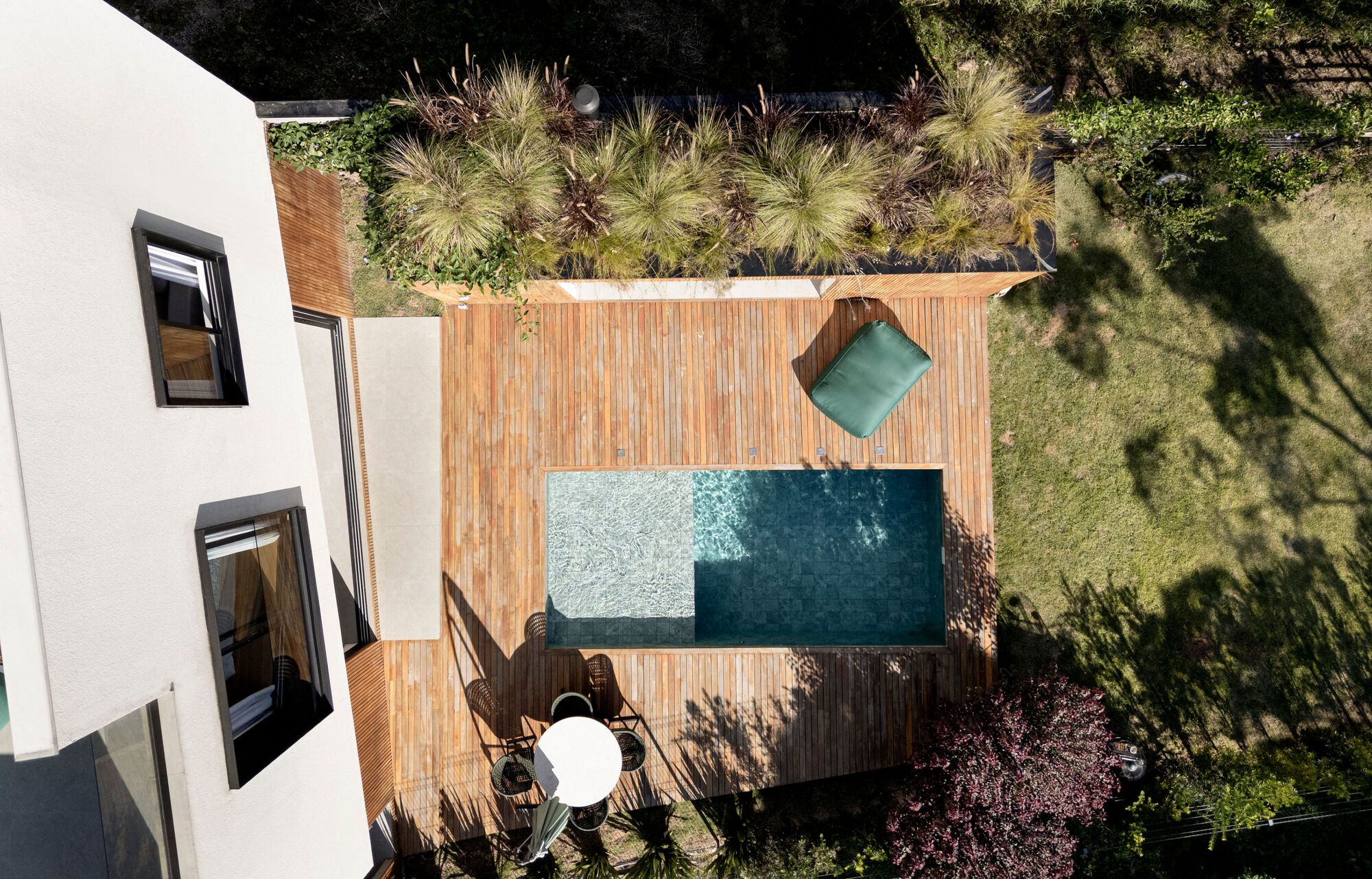 Top-down view of a rectangular pool set in a timber deck beside a planted green roof and lawn