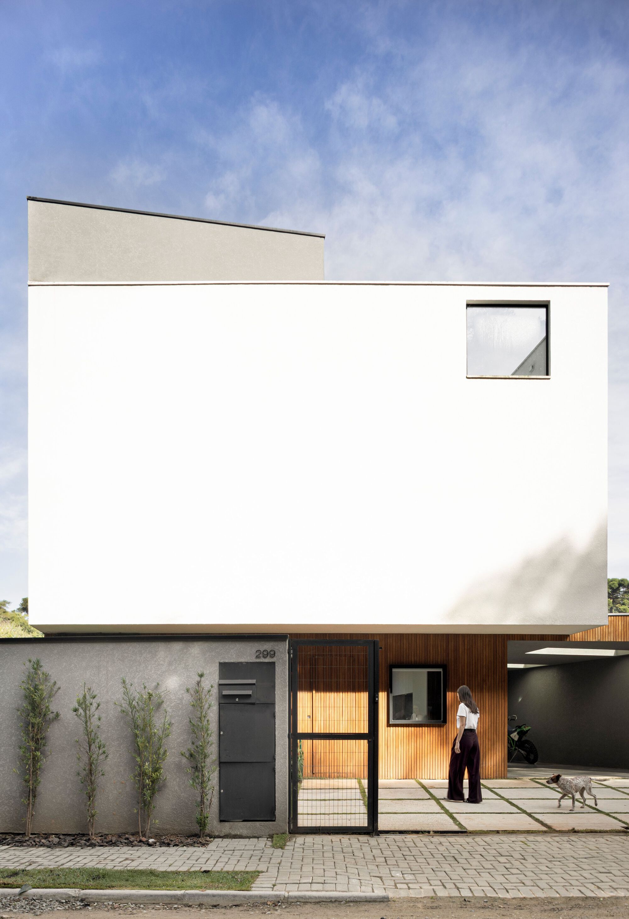 Front elevation of the white box with a square window, a woman and dog standing at the gate