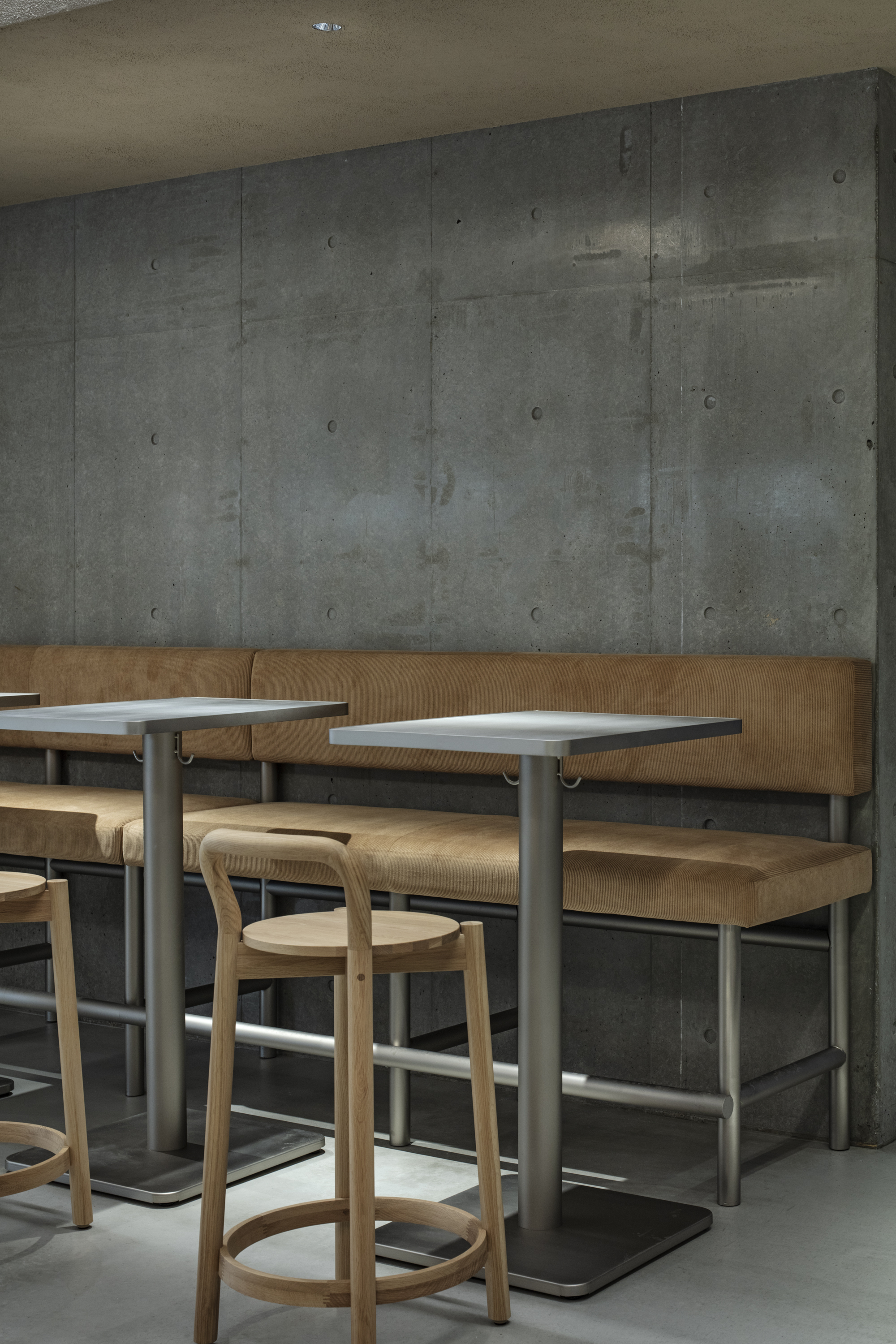 Close-up of the tan leather bench, steel pedestal tables and a bentwood stool against the board-formed concrete wall