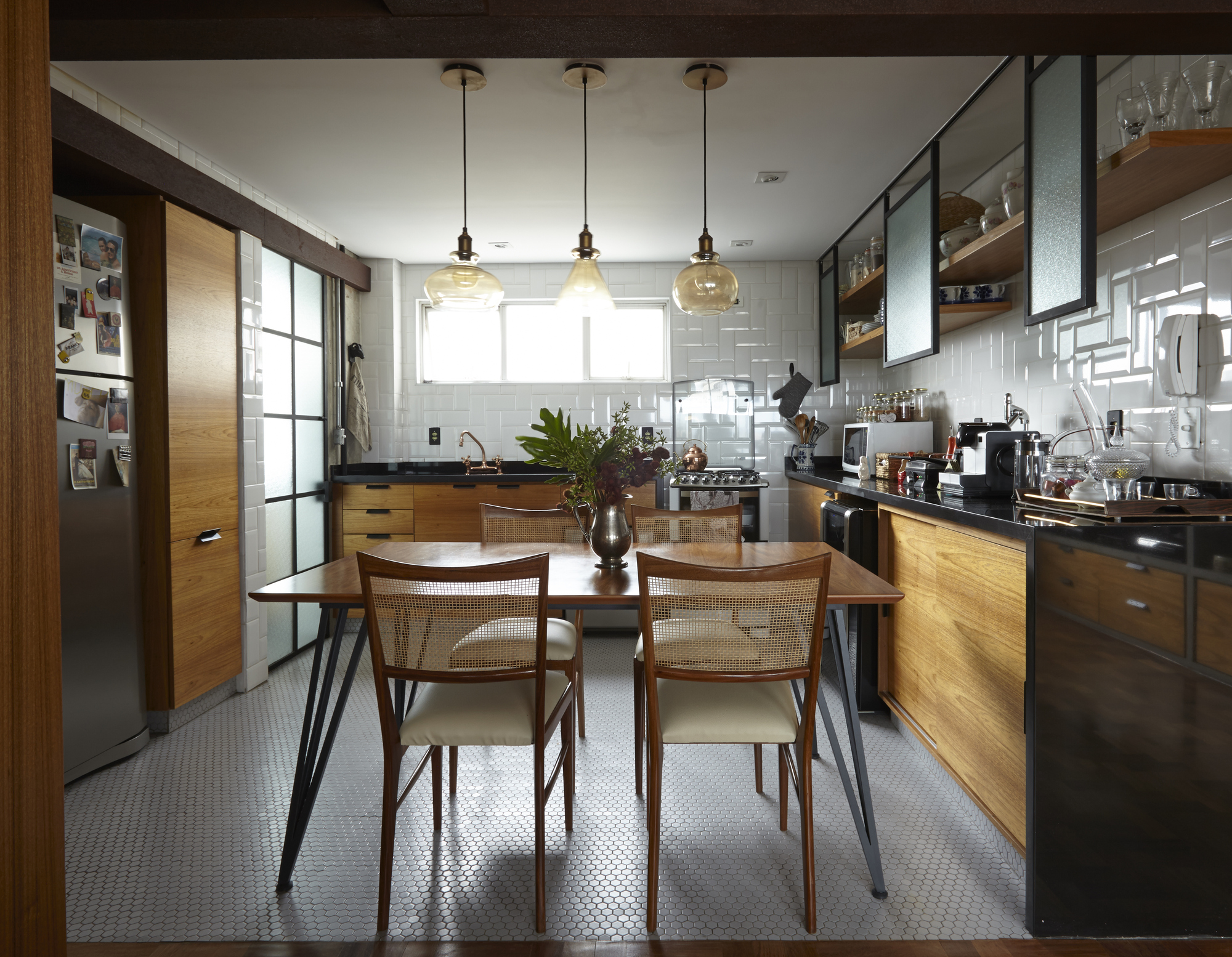 Kitchen and dining area with three amber glass pendants, black steel-framed cabinets and timber counters under a bright window