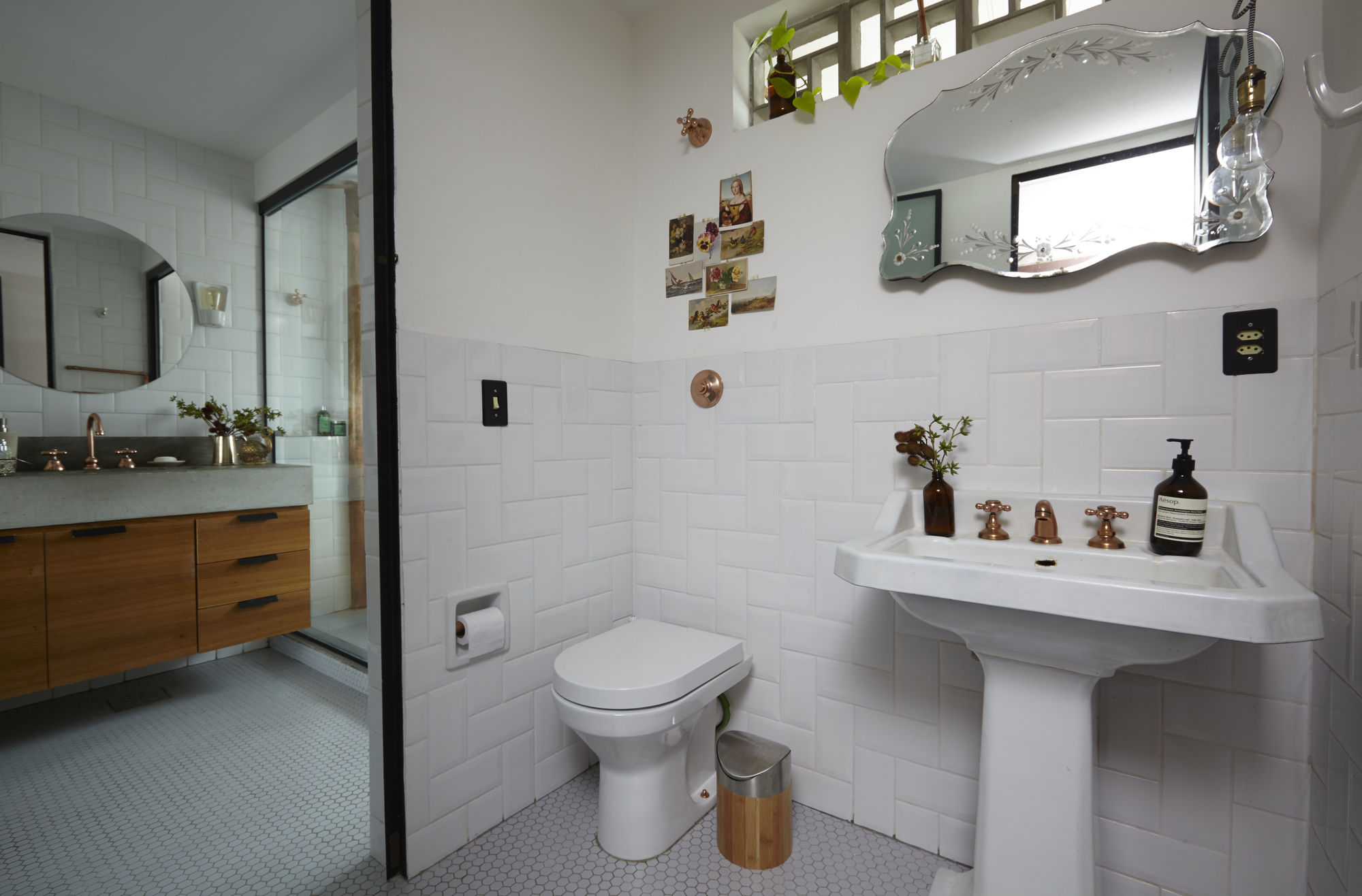 Bathroom with white subway tile walls, pedestal sink with copper taps, and a scalloped mirror under a small clerestory window