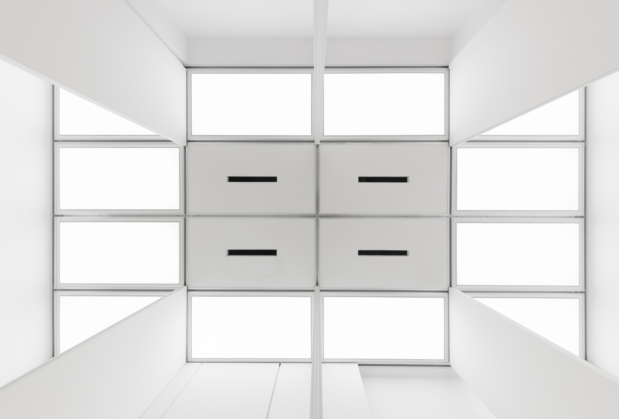 Upward view of the ceiling grid of glowing translucent panels and four solid gray panels with black slot vents