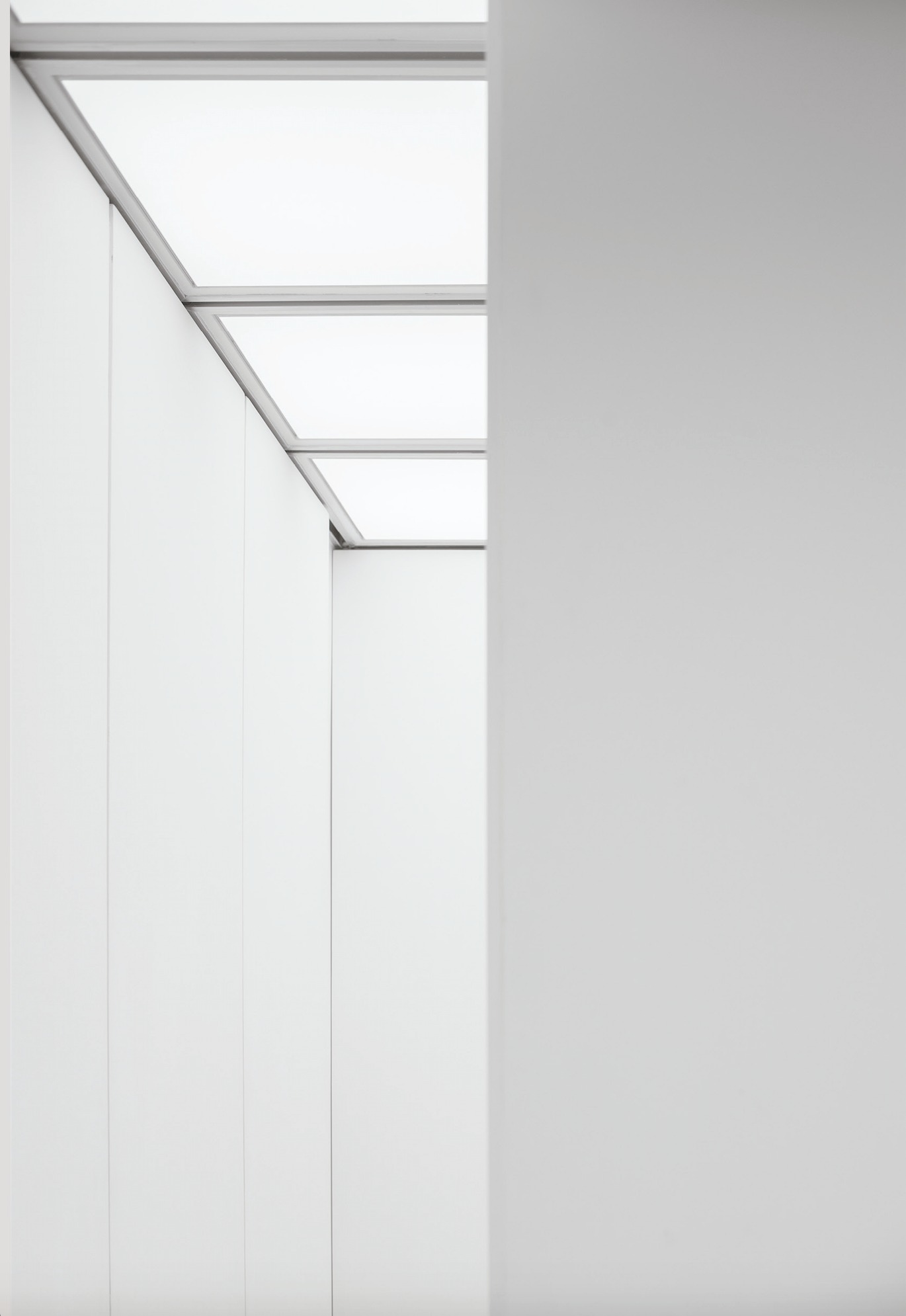 Close view of vertical white wall panels meeting a gridded luminous ceiling, with a plain grey wall plane at right