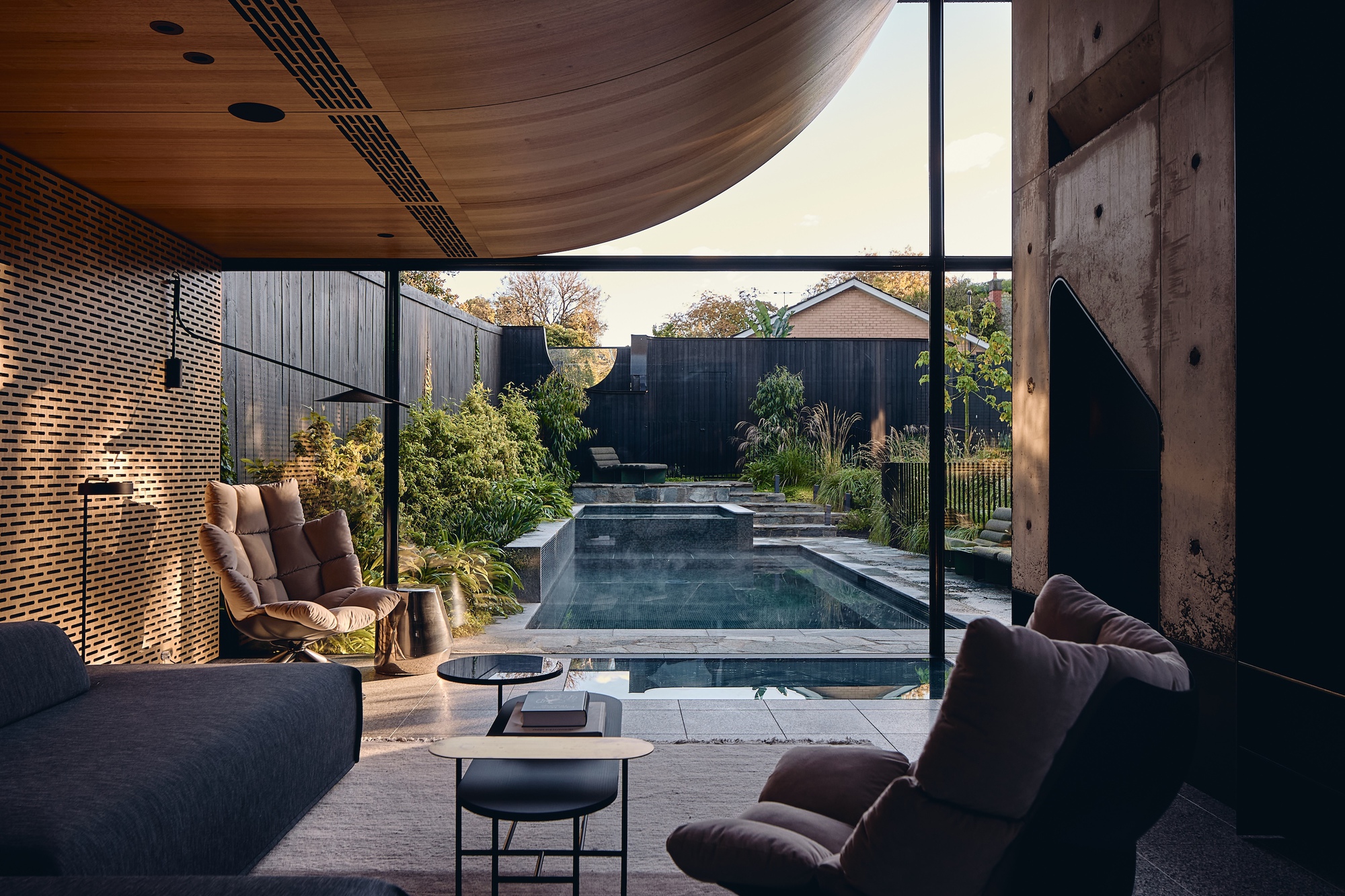 Living room opening through floor-to-ceiling glass to a plunge pool, with a curved timber ceiling and perforated brick wall
