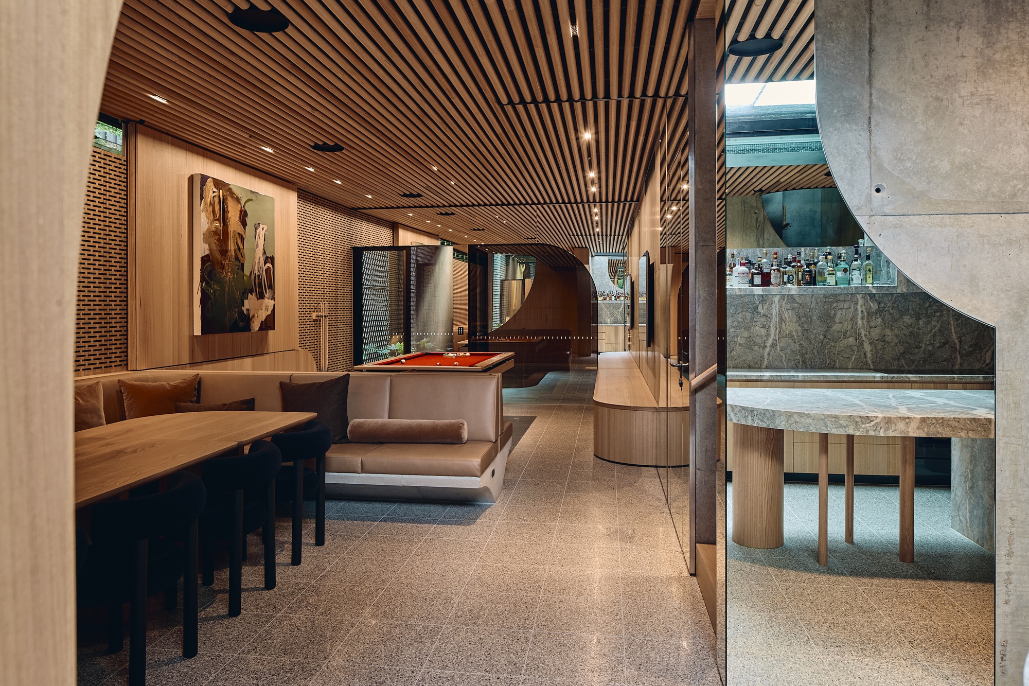 Long entertainment room with a slatted timber ceiling, built-in banquette, red pool table and mirrored bar glimpsed through a curved opening